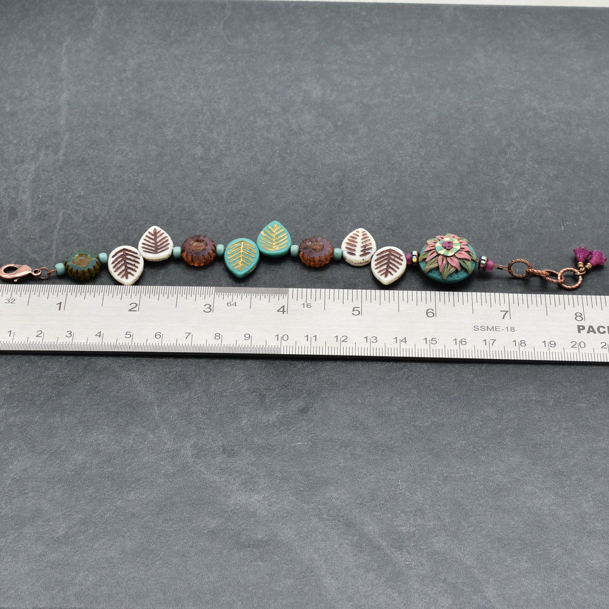 Beaded bracelet with decorative elements on a gray surface with a ruler for scale.