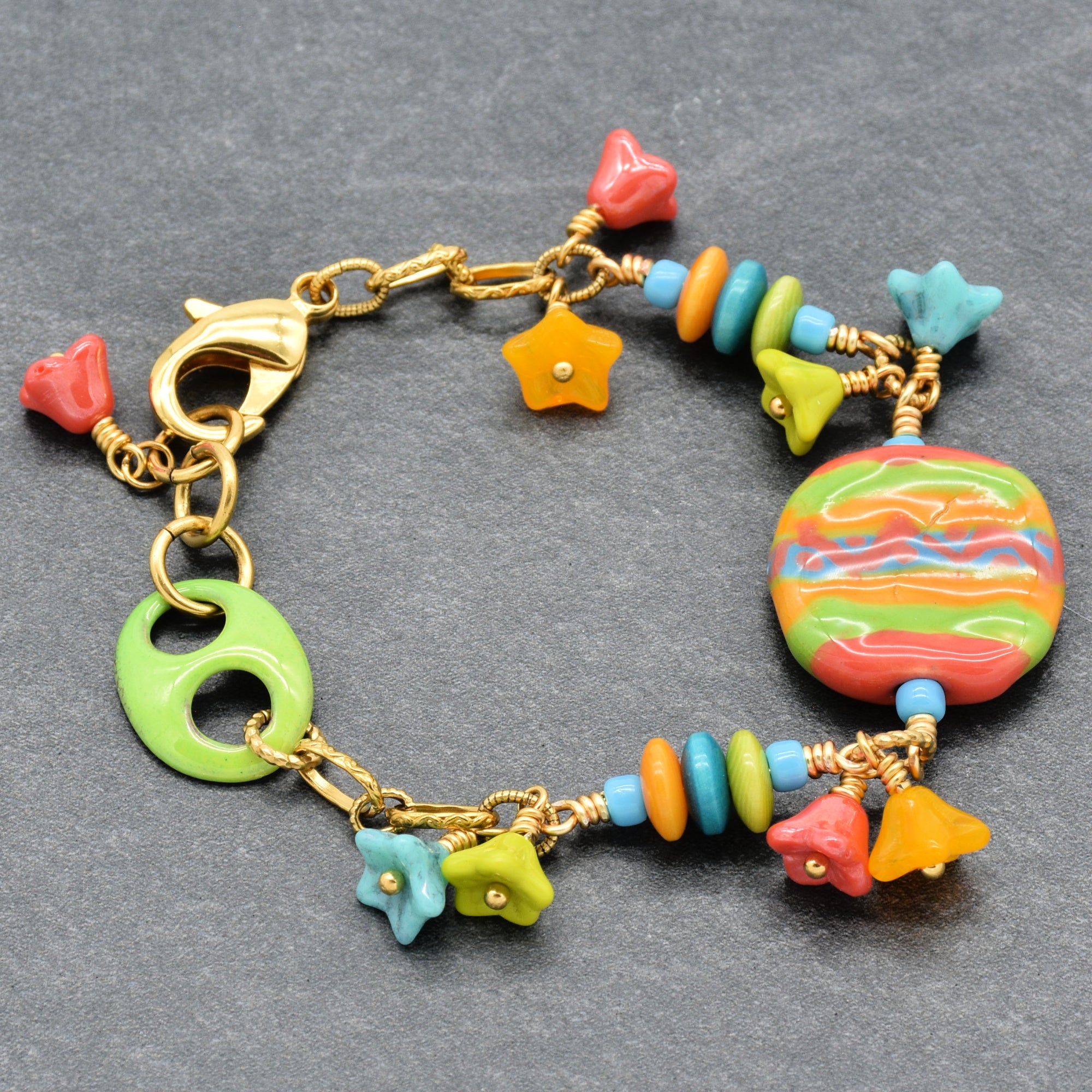 Happy colorful bracelet with African Kazuri focal, tagua nuts, and Czech glass flowers in tangerine, lime, marigold and turquoise on a gray surface - handmade with love by Ruby Acorn