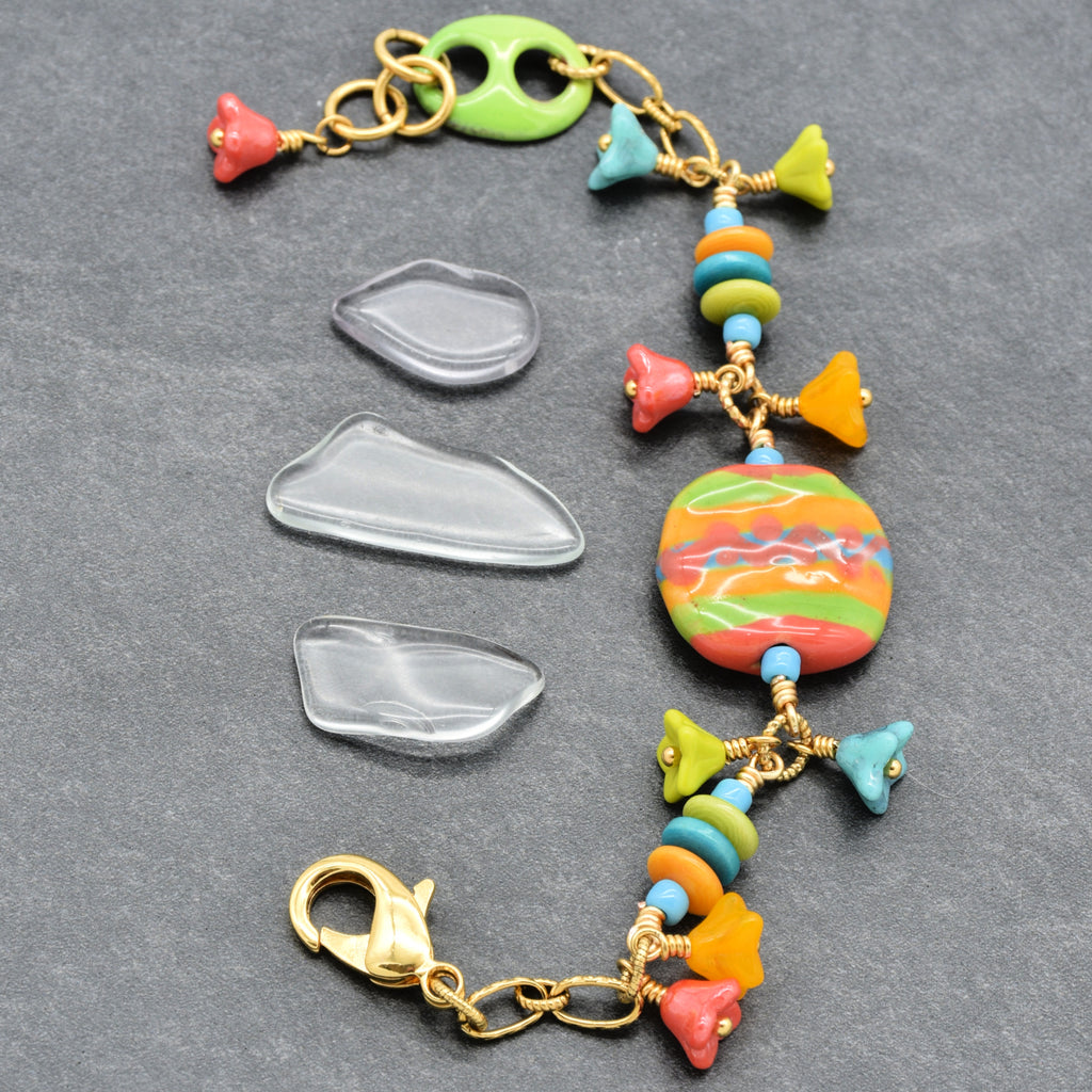 Happy colorful bracelet with African Kazuri focal, tagua nuts, and Czech glass flowers in tangerine, lime, marigold and turquoise on a gray surface - handmade with love by Ruby Acorn