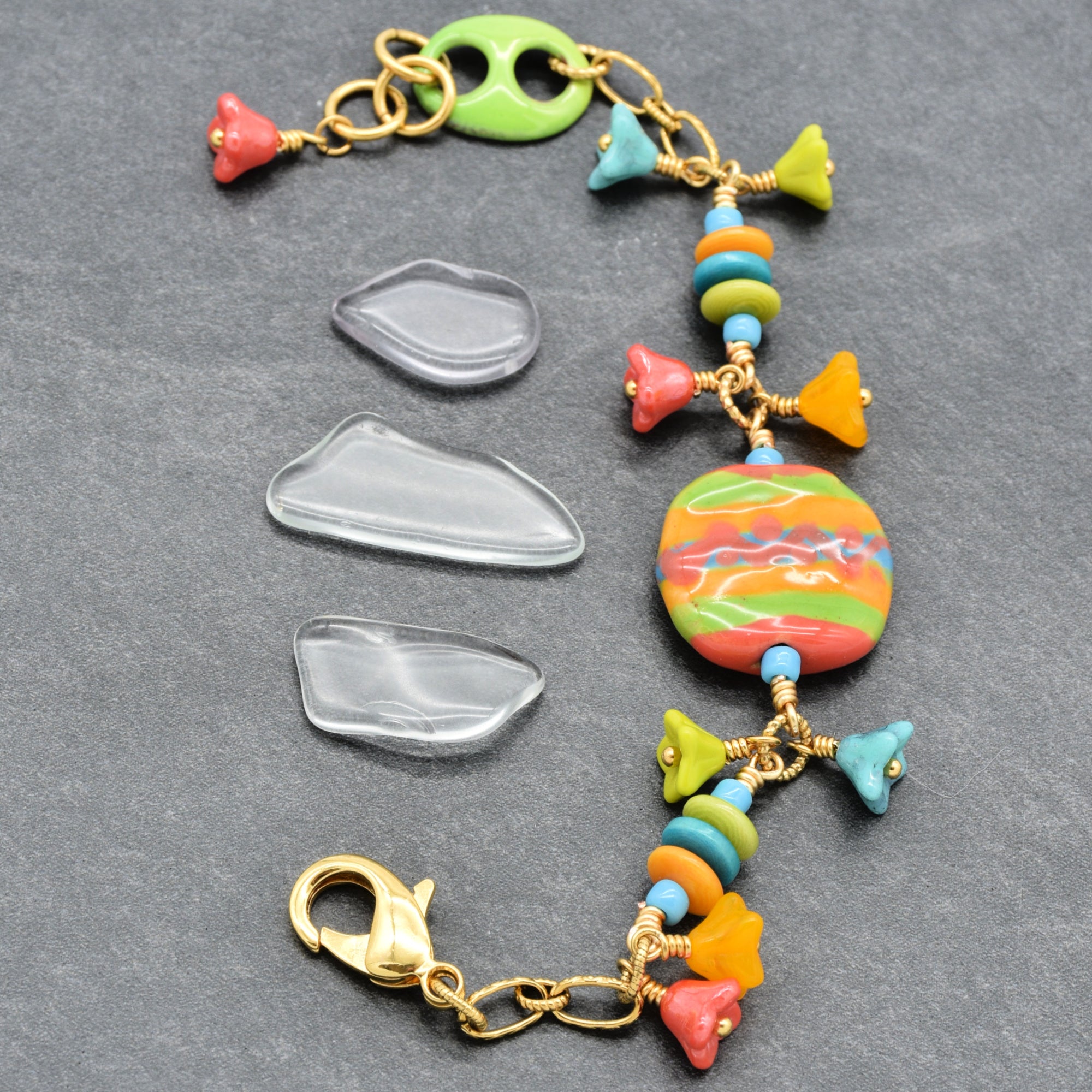 Happy colorful bracelet with African Kazuri focal, tagua nuts, and Czech glass flowers in tangerine, lime, marigold and turquoise on a gray surface - handmade with love by Ruby Acorn
