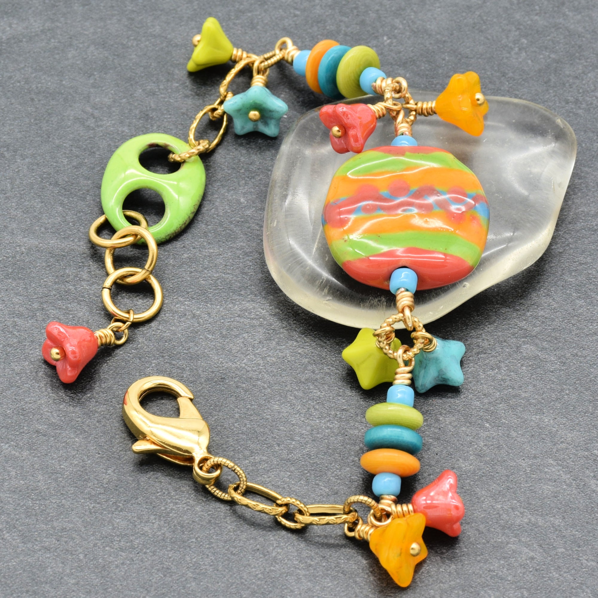 Happy colorful bracelet with African Kazuri focal, tagua nuts, and Czech glass flowers in tangerine, lime, marigold and turquoise on a gray surface - handmade with love by Ruby Acorn