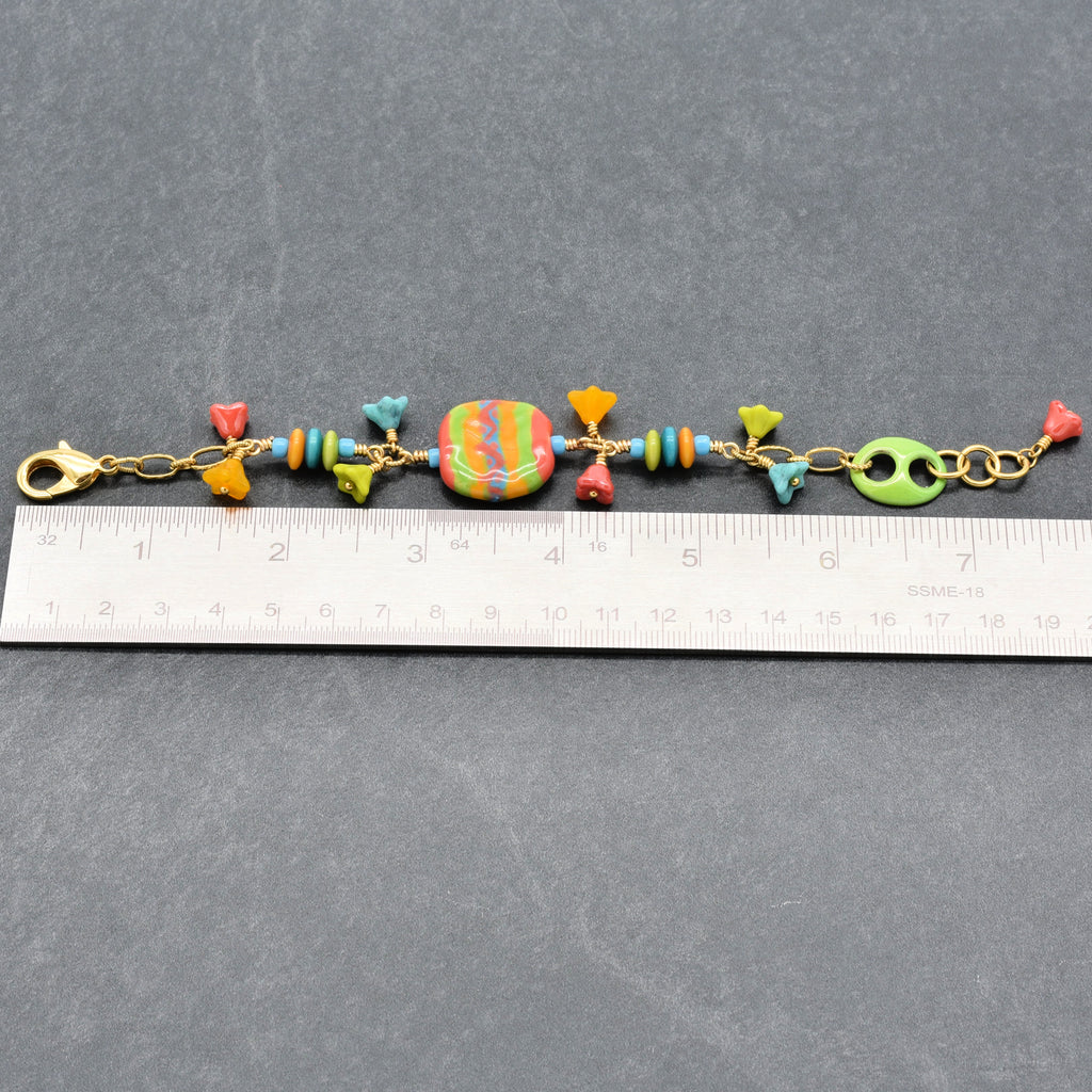 Happy colorful bracelet with African Kazuri focal, tagua nuts, and Czech glass flowers in tangerine, lime, marigold and turquoise next to a ruler for scale - handmade with love by Ruby Acorn