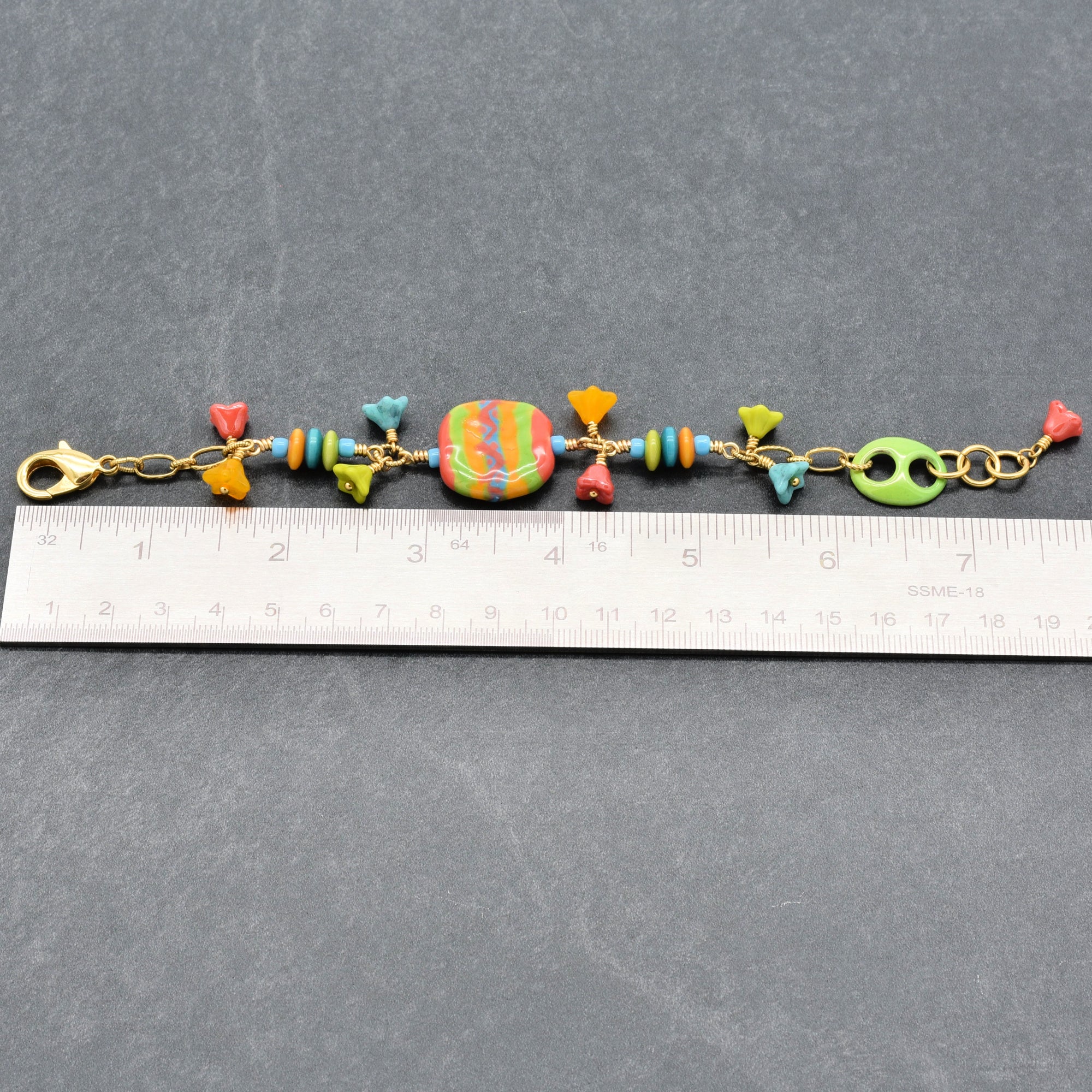 Happy colorful bracelet with African Kazuri focal, tagua nuts, and Czech glass flowers in tangerine, lime, marigold and turquoise next to a ruler for scale - handmade with love by Ruby Acorn