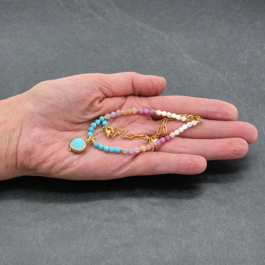 Hand holding a multi gem gold chain choker necklace with genuine turquoise focal, kunzite, peach moonstone, and more on a gray background - made with love by Ruby Acorn
