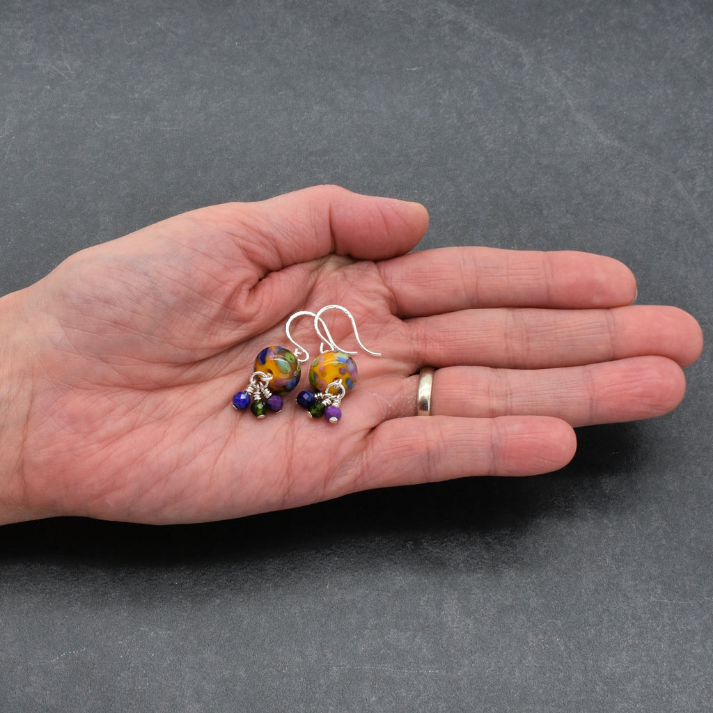 Hand holding a pair of colorful beaded earrings against a gray background