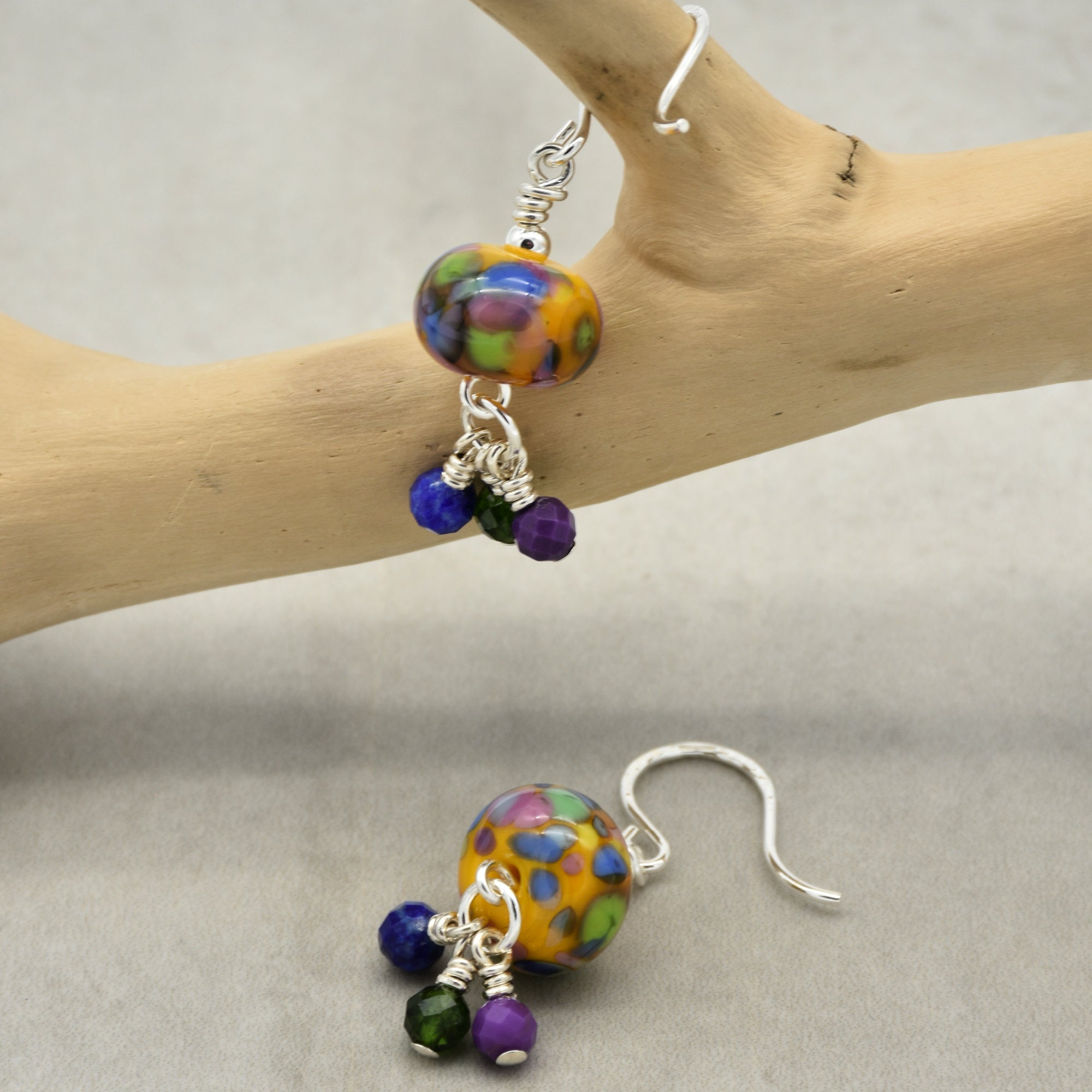 Colorful beaded earrings on a wooden branch with a neutral background