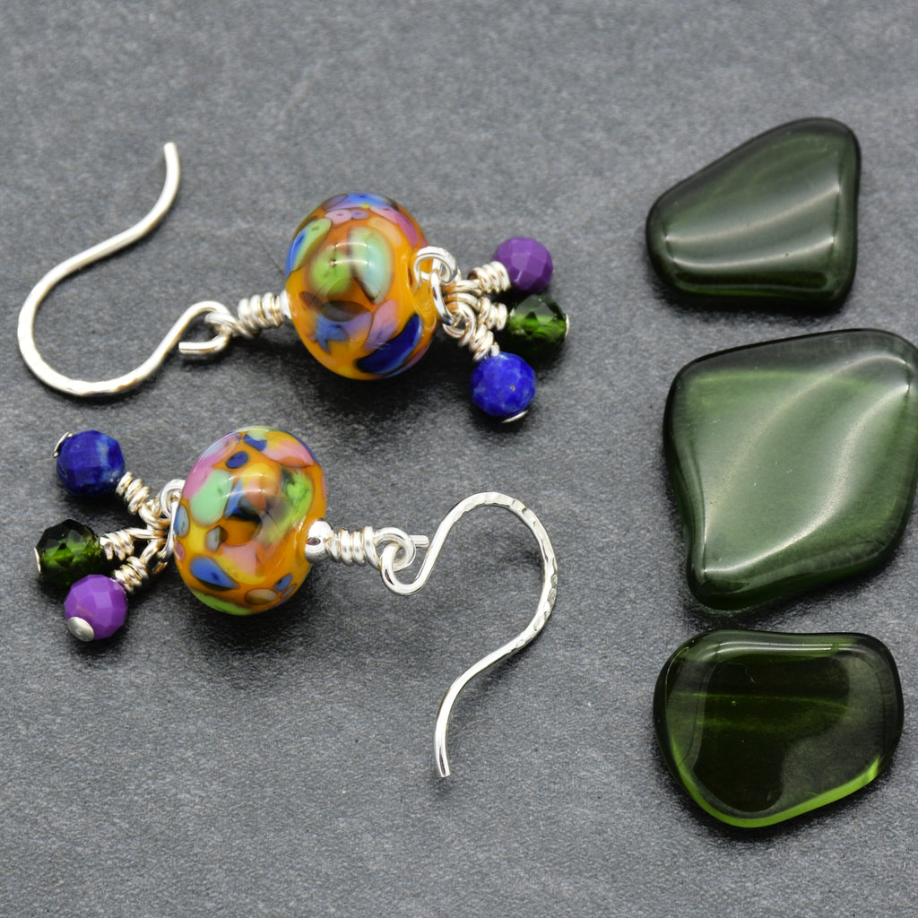 Colorful beaded earrings on a gray surface with green stones.