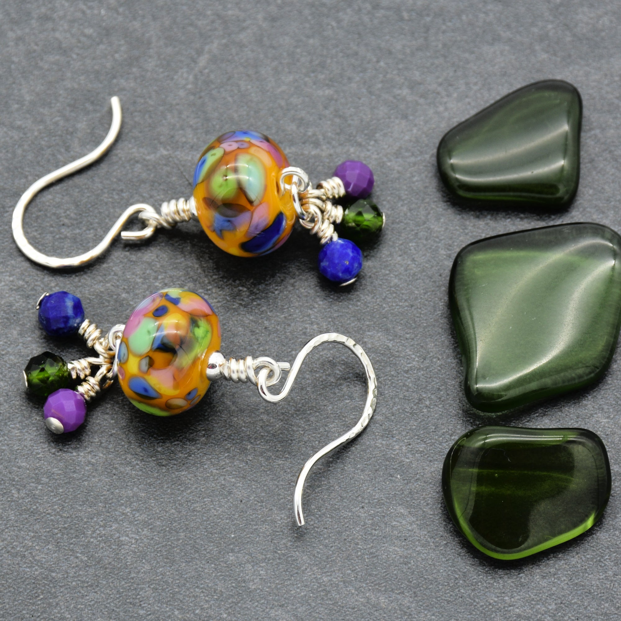 Colorful beaded earrings on a gray surface with green stones.
