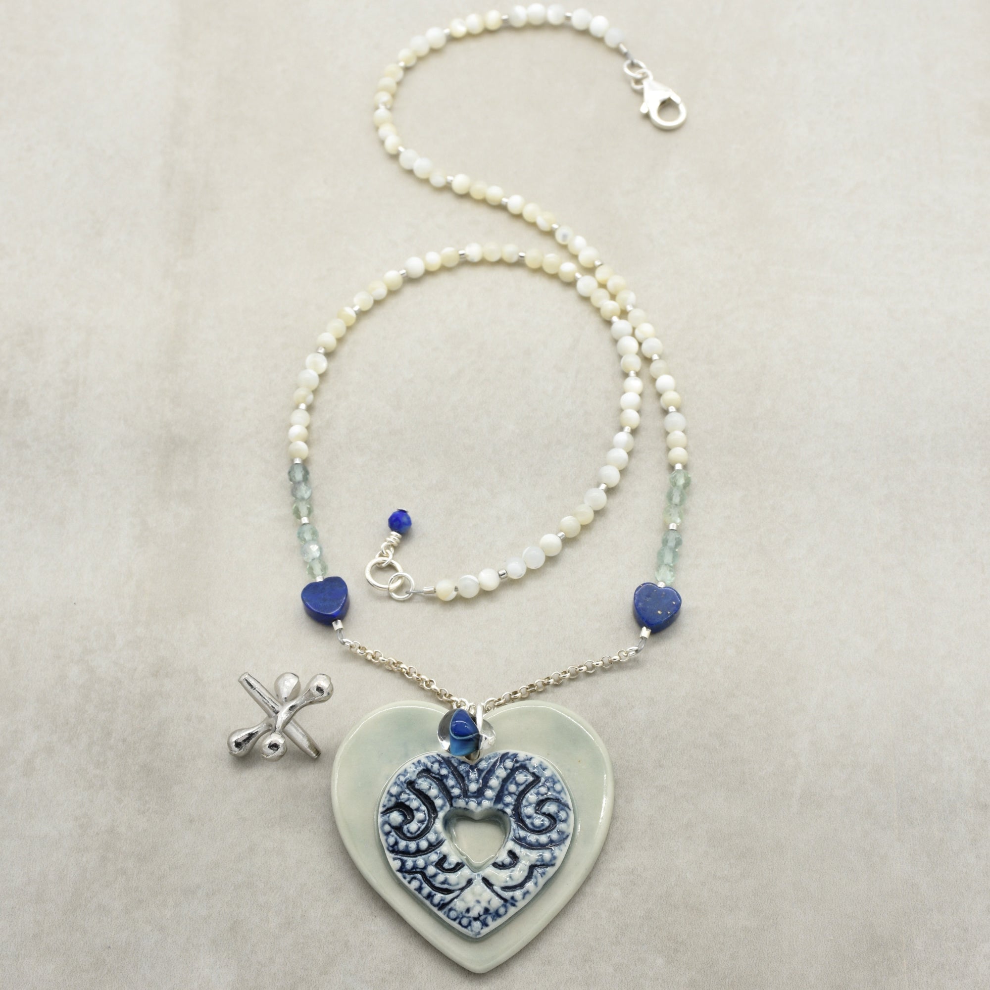 Necklace with heart-shaped ceramic pendant and blue beads on a beige background