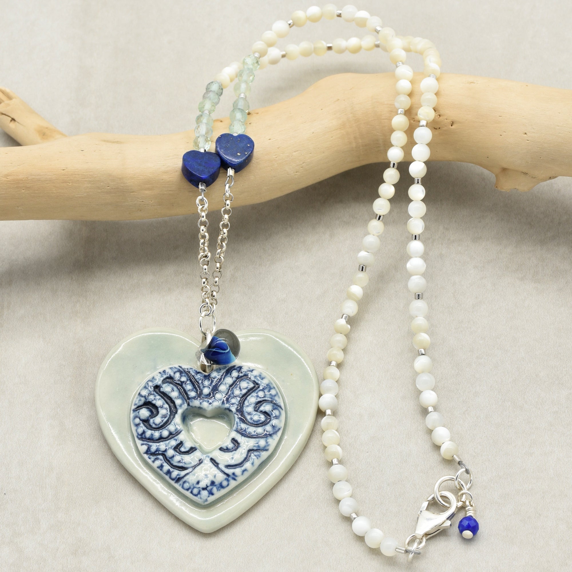 Necklace with heart-shaped ceramic pendant and white beads on a beige background