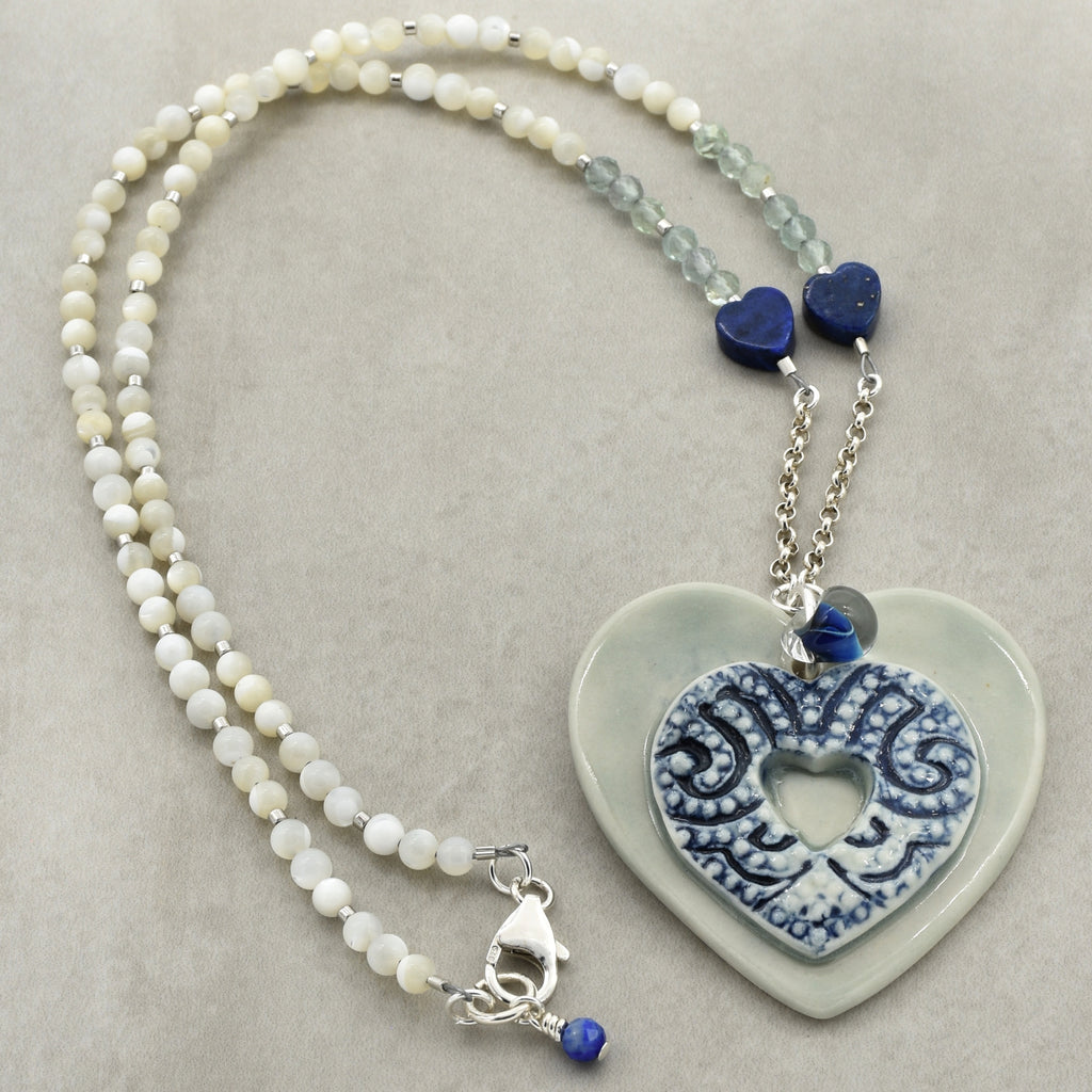 Necklace with heart-shaped pendant and beaded chain on a neutral background