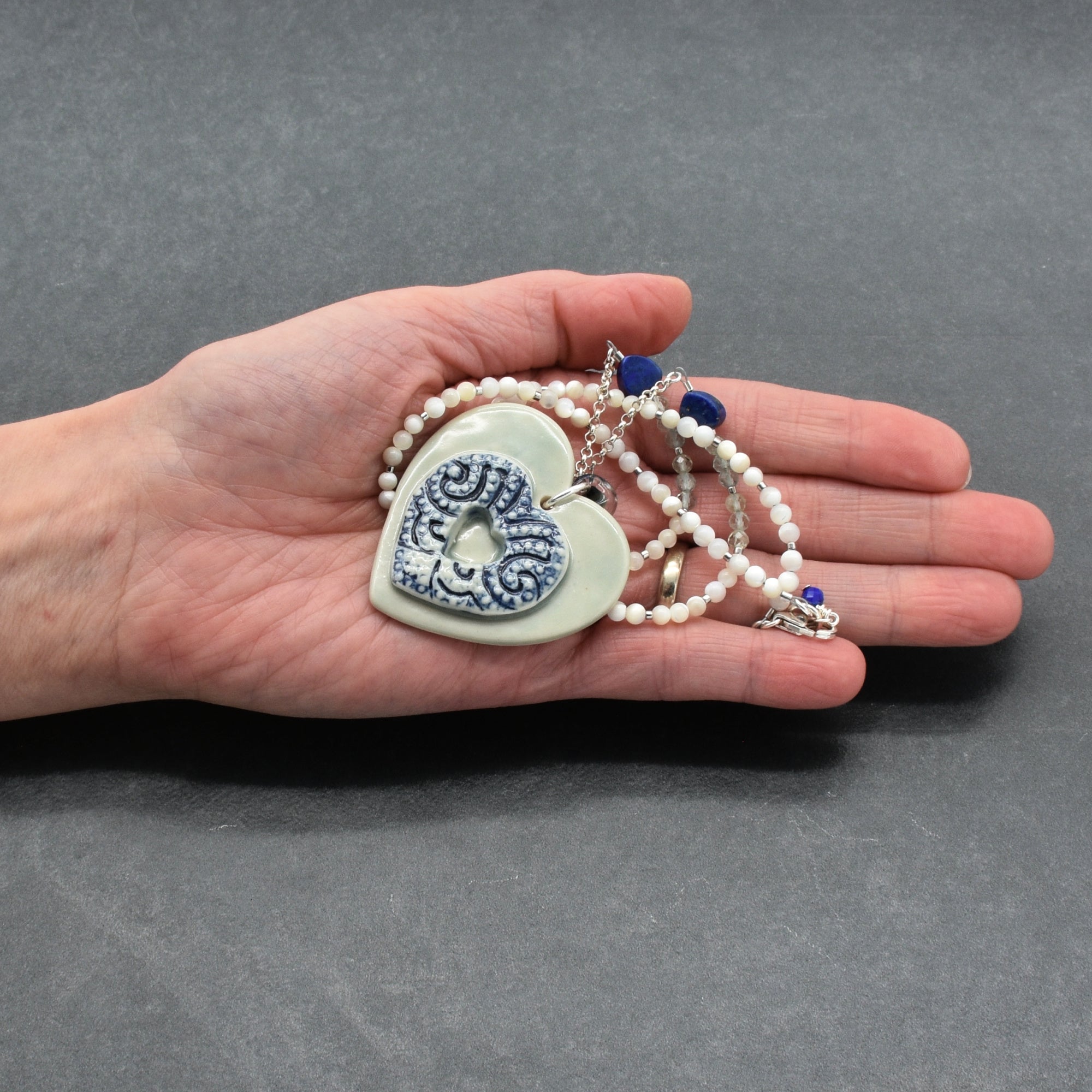Hand holding a necklace with a heart-shaped pendant against a gray background