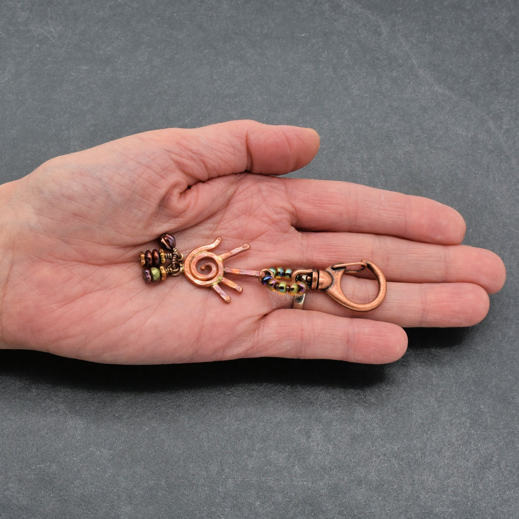 Hand holding a small, intricately designed keychain against a gray background