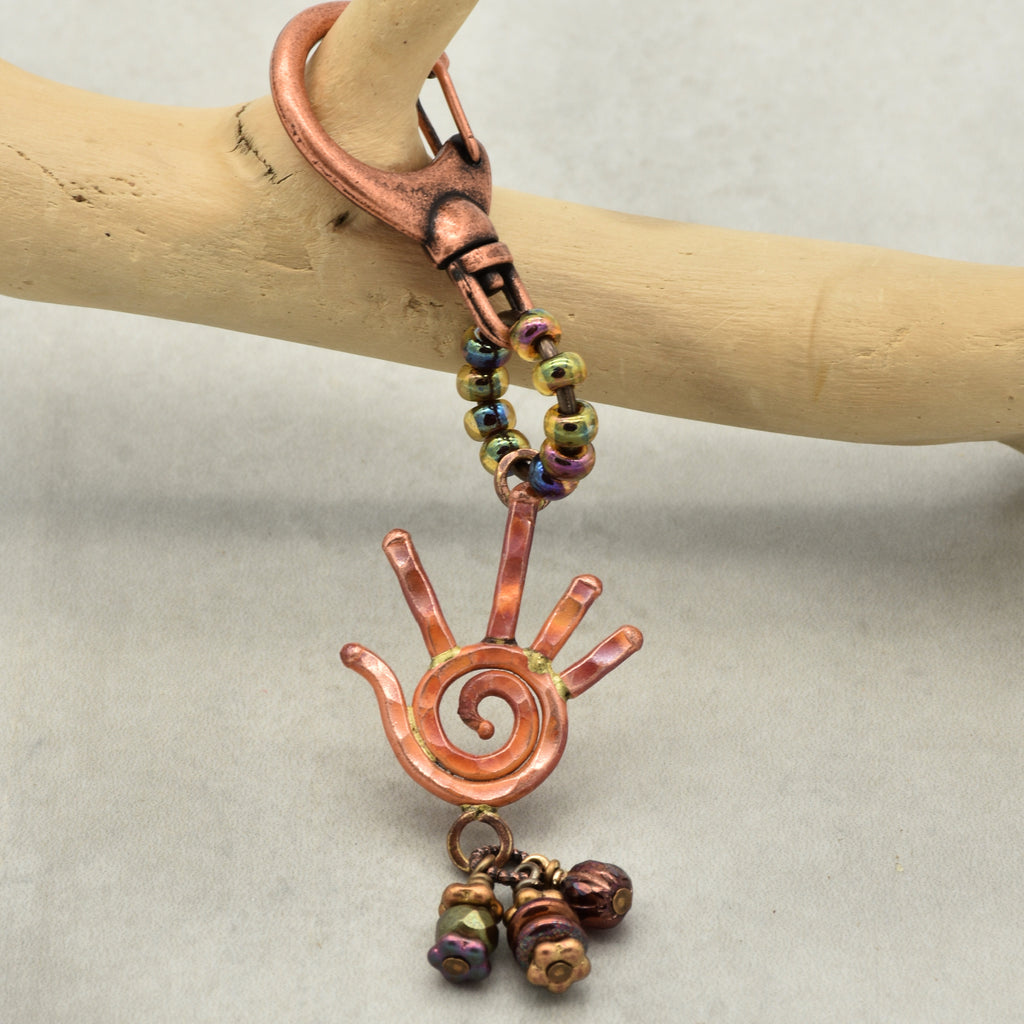 Copper keychain with spiral design and beads on a wooden stick against a light background