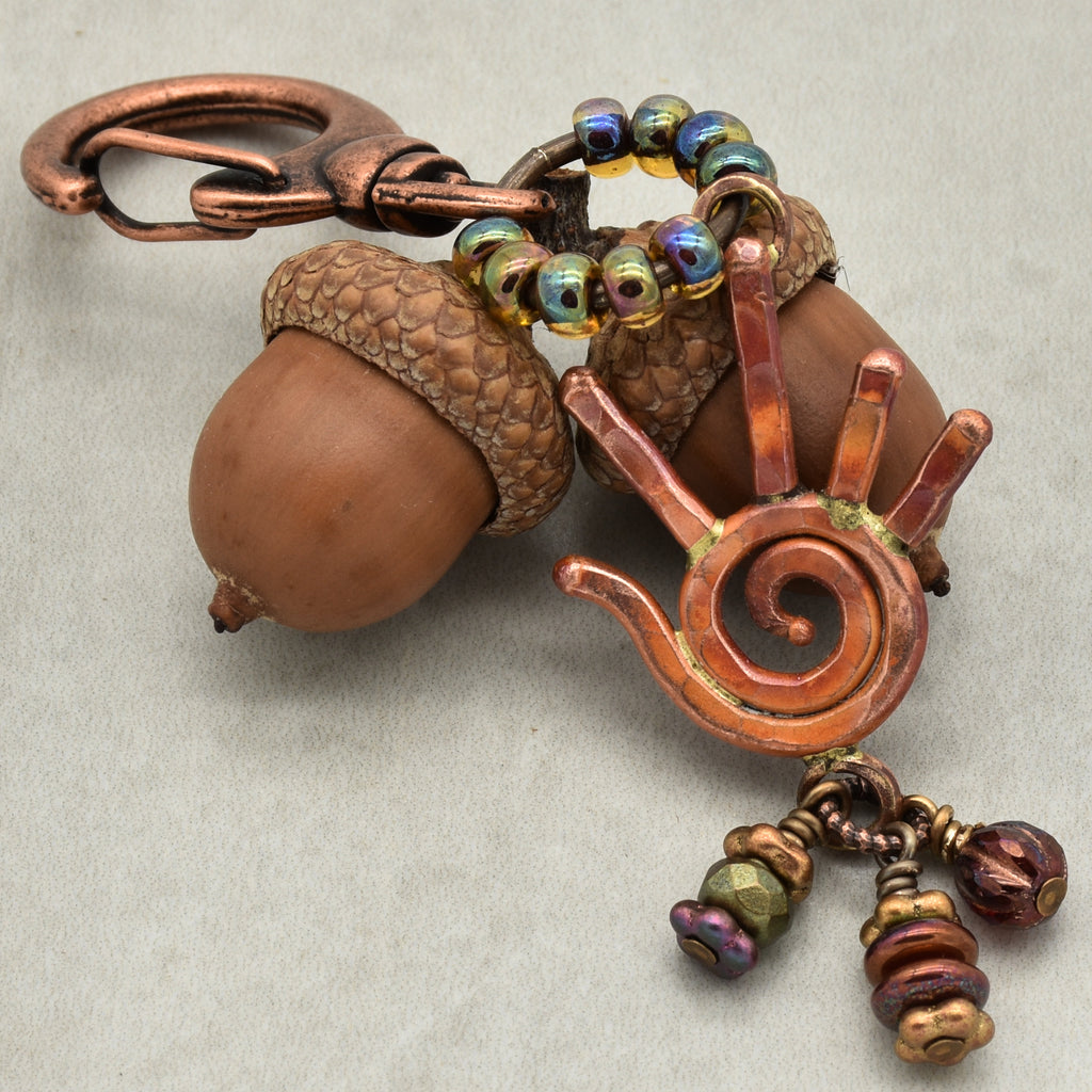 Decorative keychain with acorn and spiral design on a neutral background