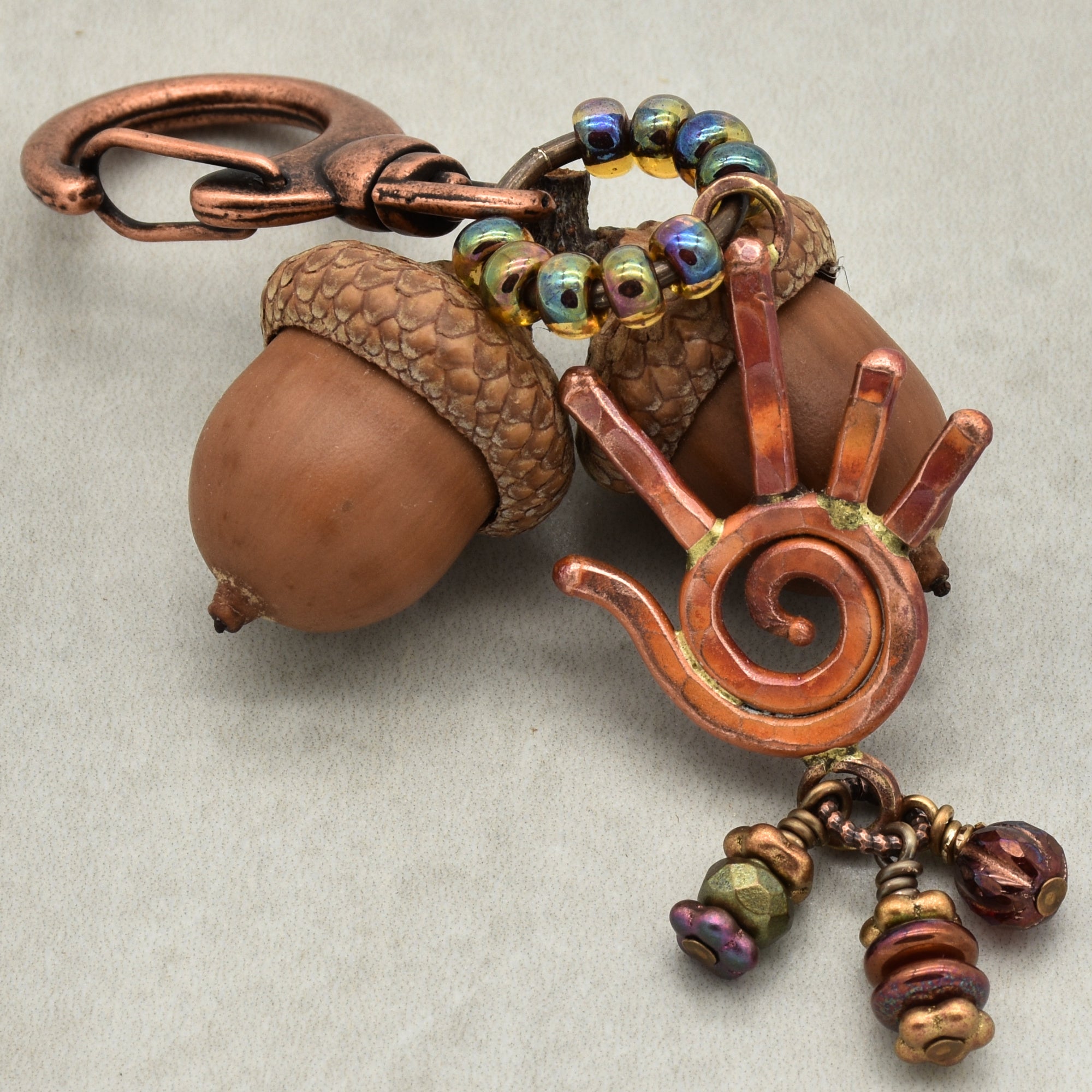 Decorative keychain with acorn and spiral design on a neutral background