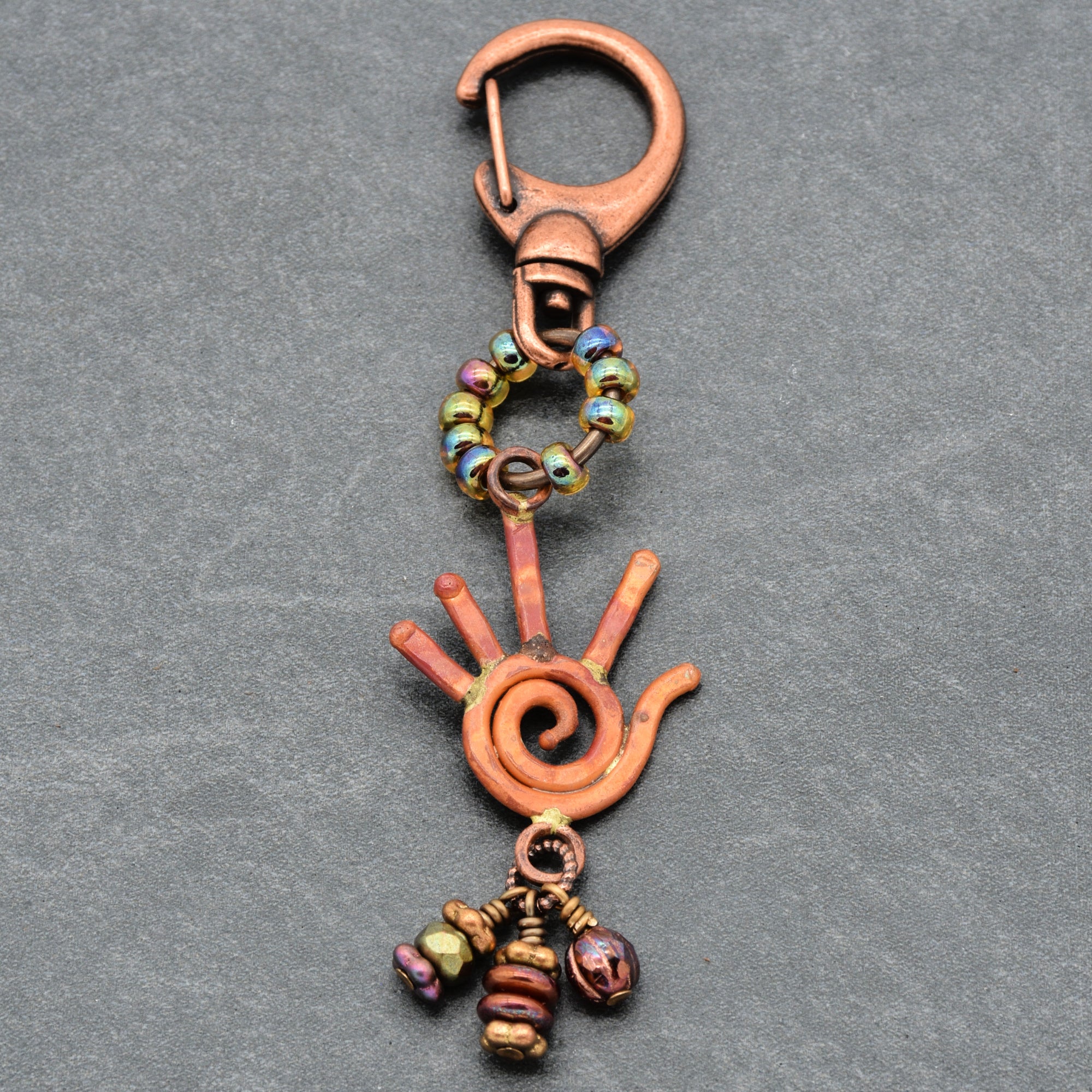Decorative keychain with hand design and beads on a gray background