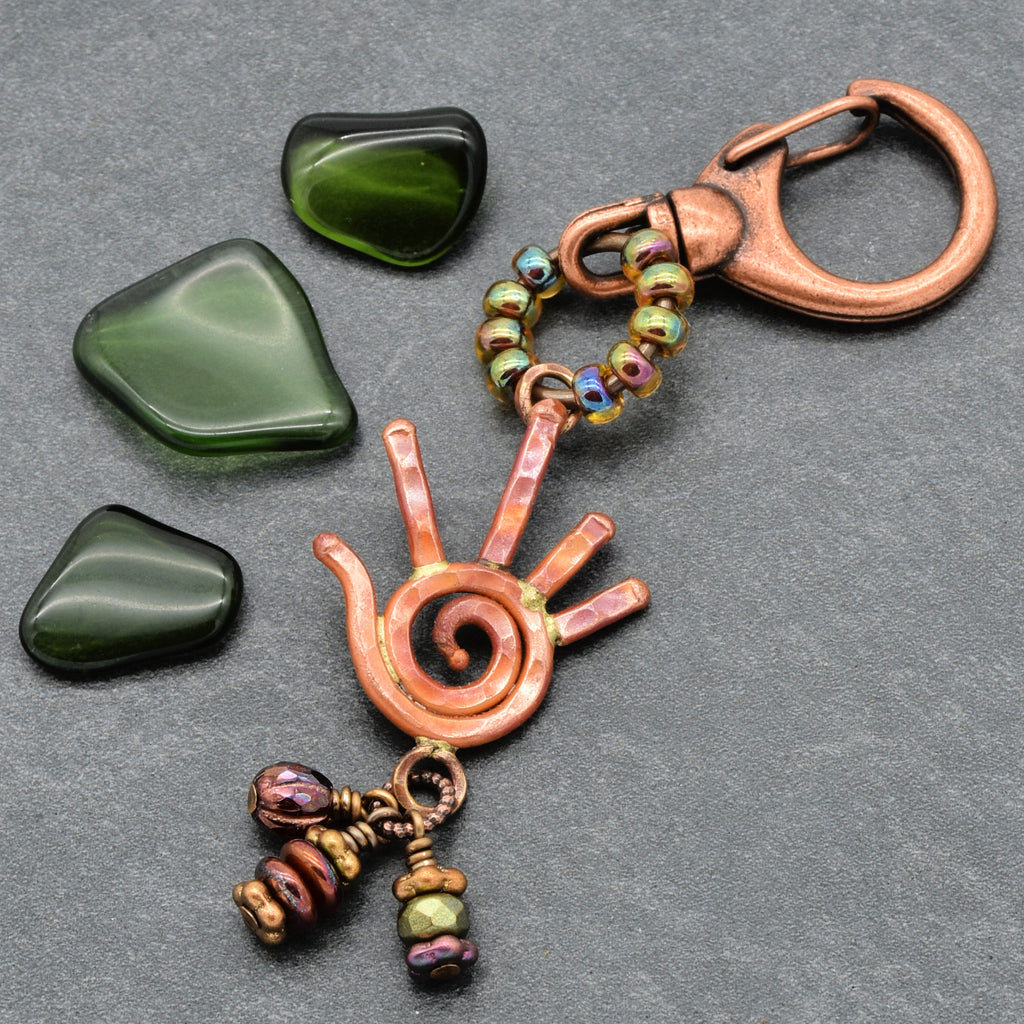 Copper keychain with spiral design and beads on a gray surface with green stones.