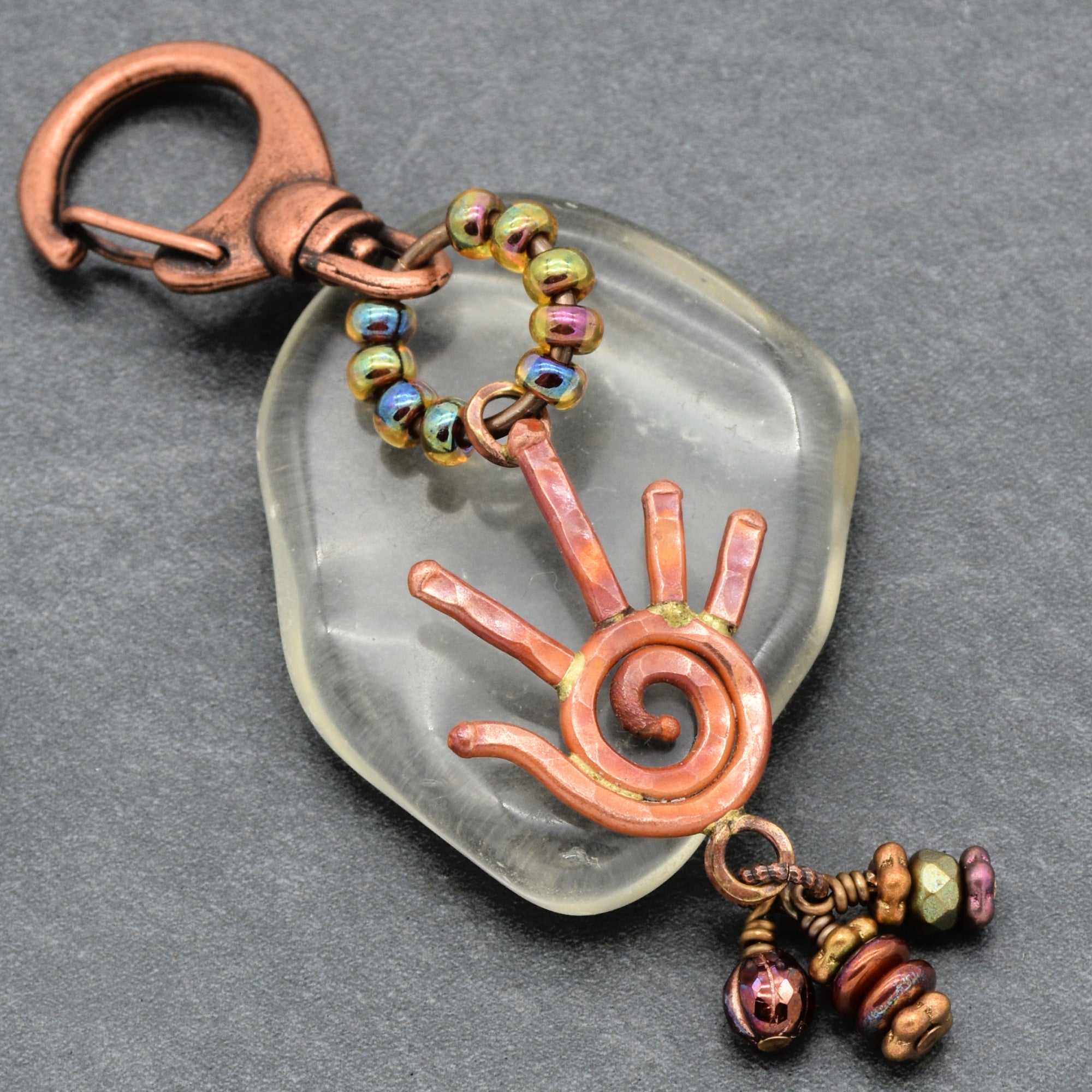 Decorative keychain with spiral design and beads on a gray background