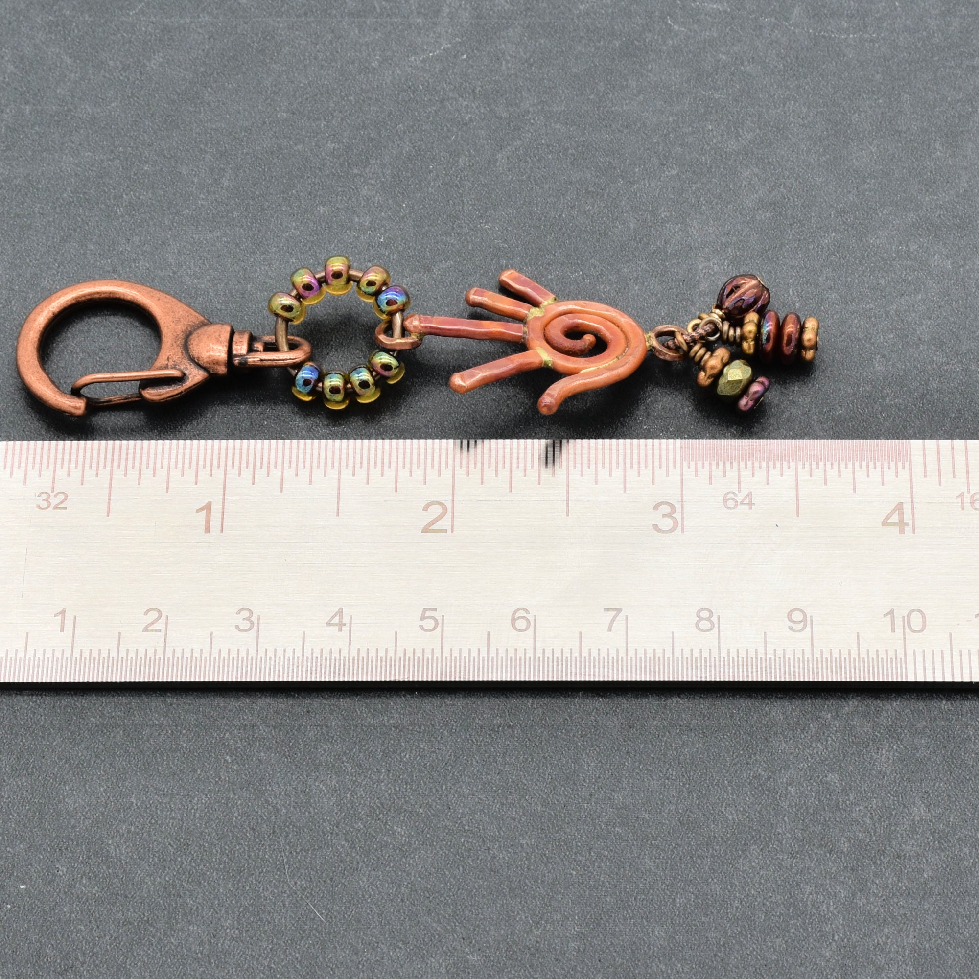 Decorative keychain with beads and hand design on a gray background with a ruler for scale.