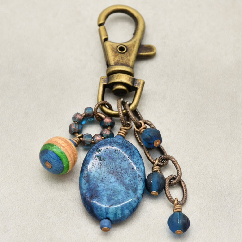 An antique bronze-toned lobster clasp keychain featuring a large oval blue stone charm, smaller blue beads, and a striped wooden bead accent on a light gray background - made with love in Colorado by Ruby Acorn.