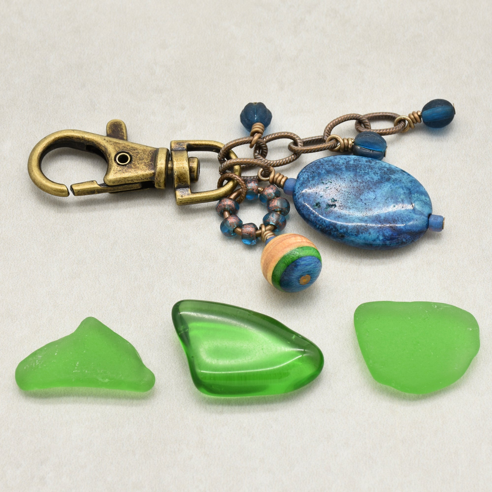 A handmade bohemian-style keychain featuring a brass clasp, blue stone beads,  and a striped skateboard bead, displayed on a light gray background - made with love in Colorado by Ruby Acorn.