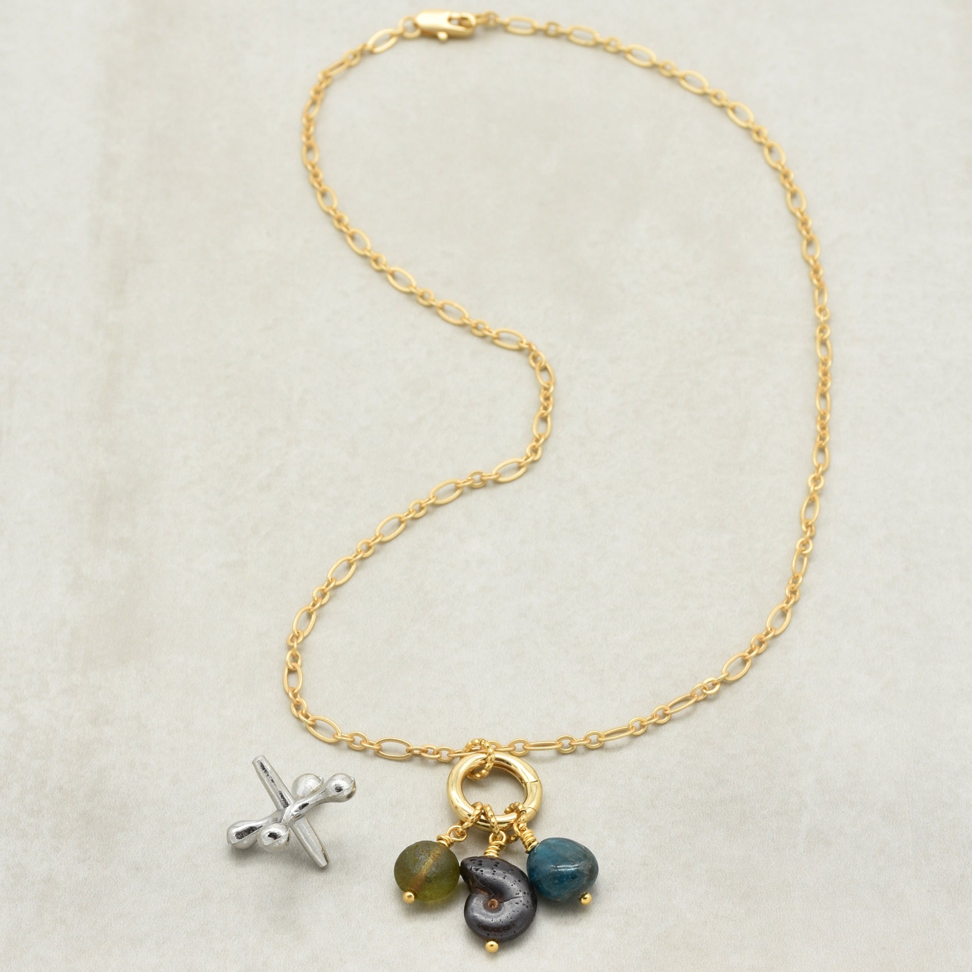 Gold chain charm necklace with brown ammonite, blue apatite, and green Czech glass on a light beige background - one of a kind art by Ruby Acorn