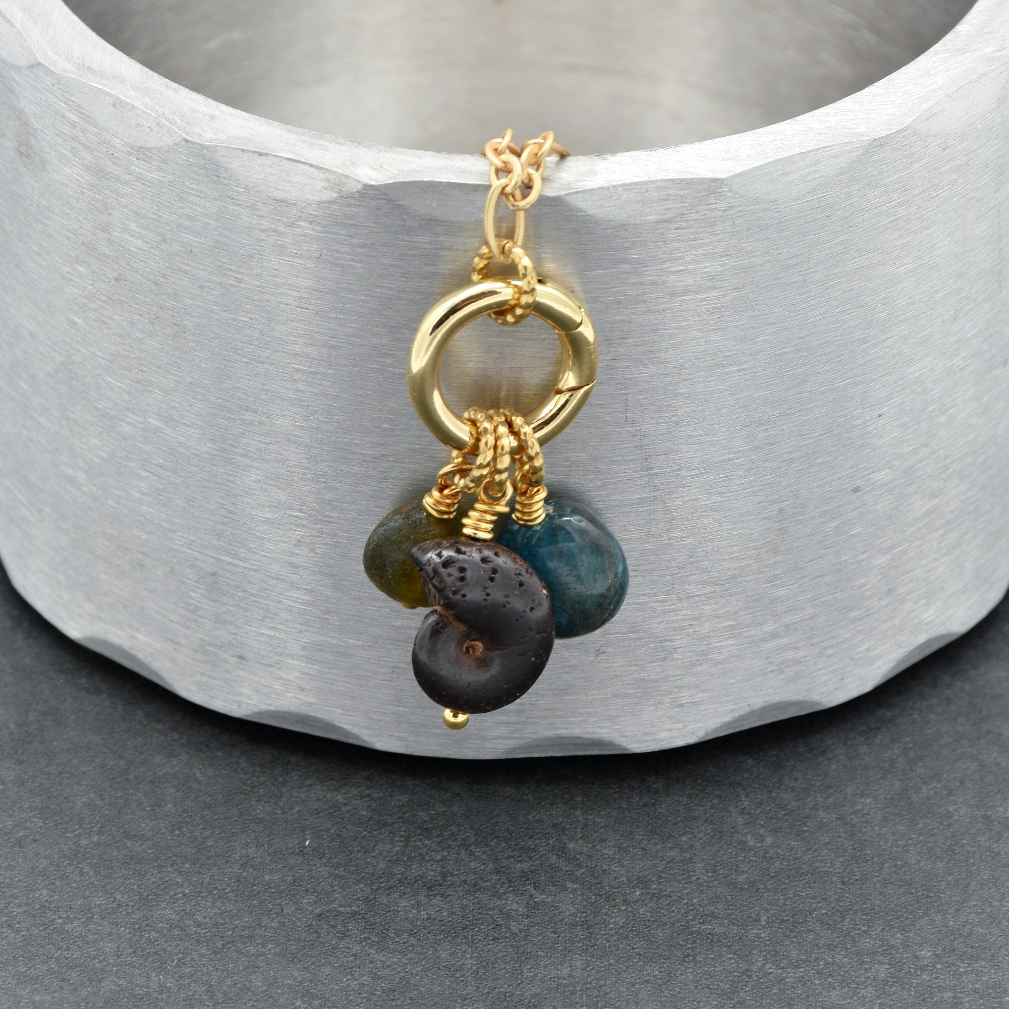 Close up of gold charm necklace  with ammonite, apatite, and Czech glass on a metallic surface - handmade with love by Ruby Acorn