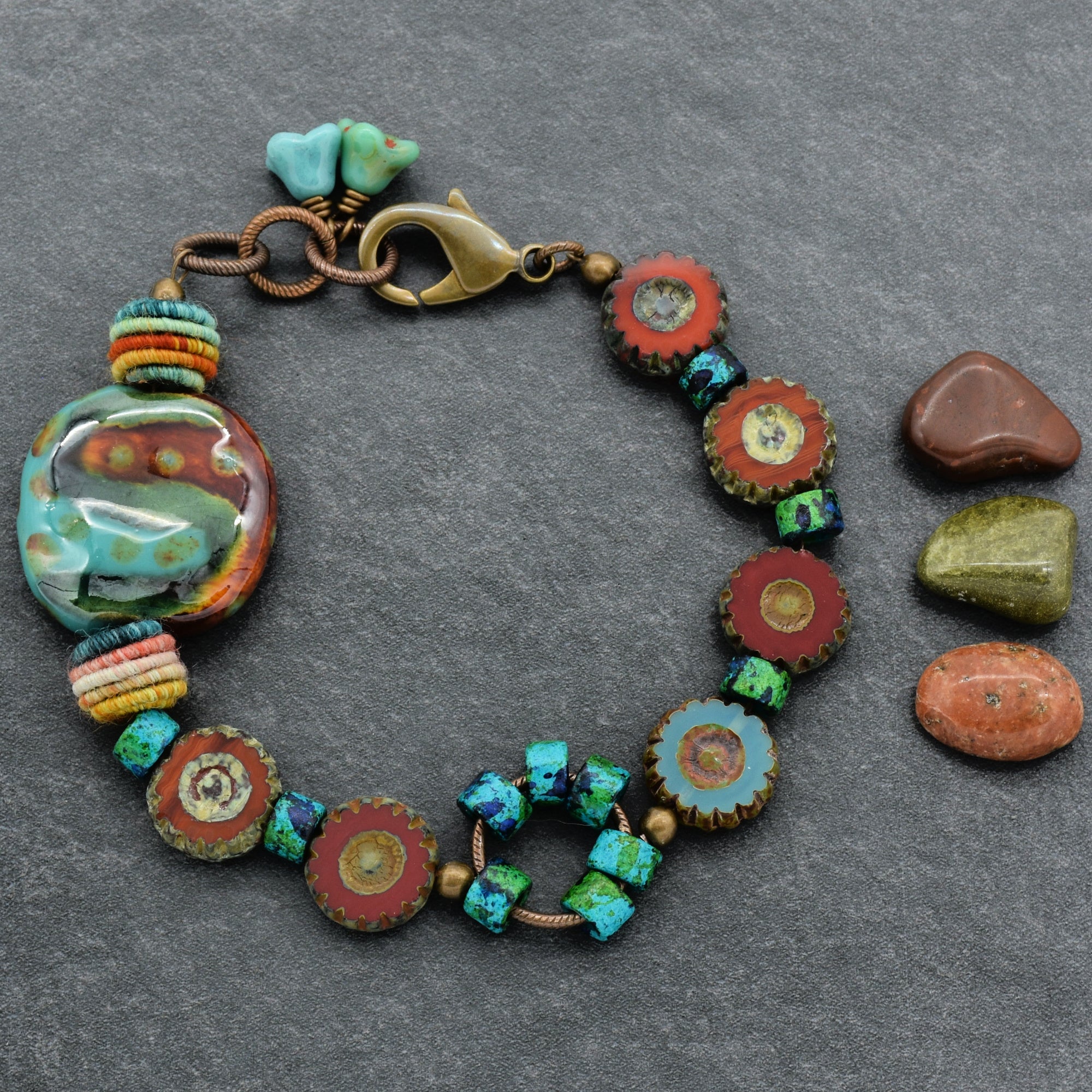 This image shows a bracelet. The jewelry piece is made up of various round and cylindrical beads, including some with intricate designs and colors in turquoise, green, and reddish tones. It also has a clasp closure, which is characteristic of bracelets.