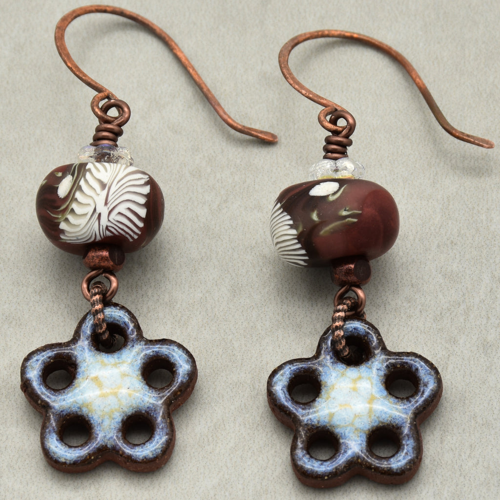 Pair of earrings with brown beads and flower-shaped charms on a beige background