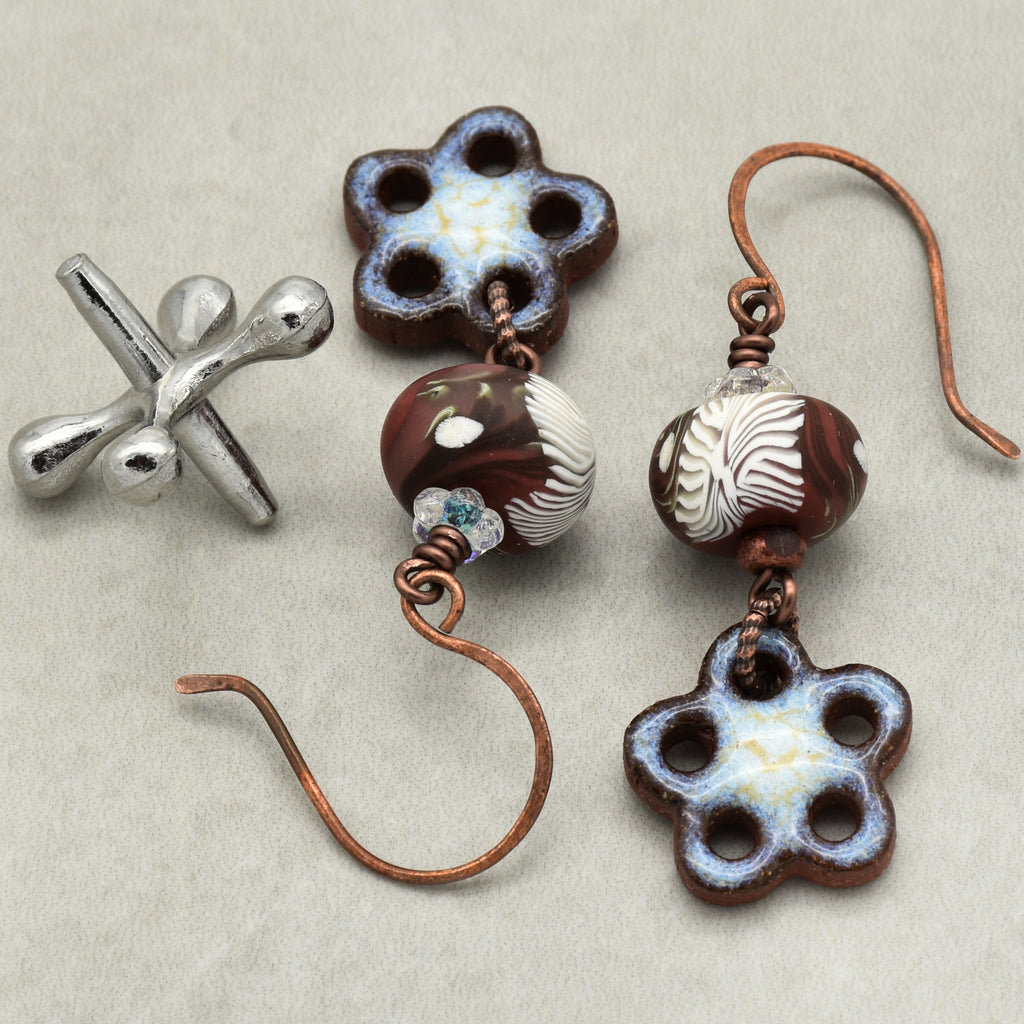 Pair of floral earrings with brown and white beads on a light gray background