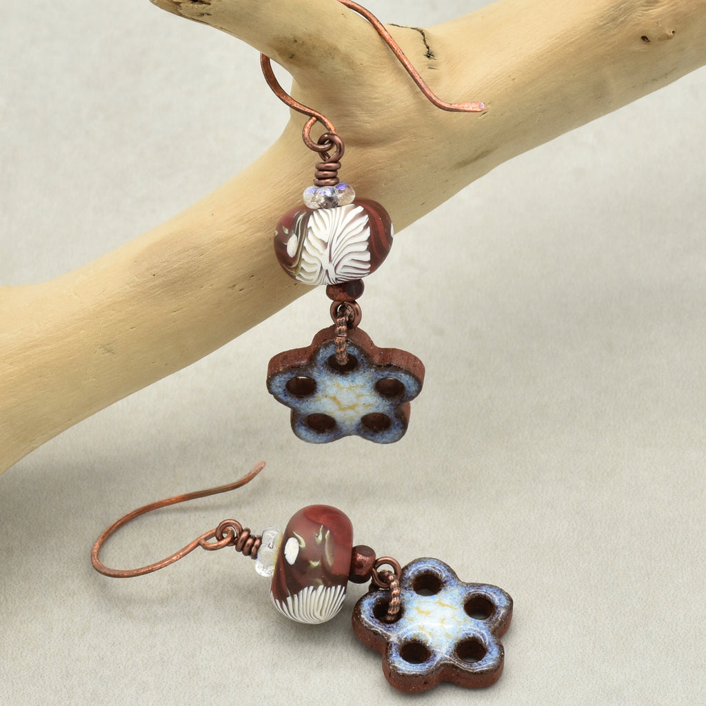 Pair of brown and white floral earrings hanging from a branch on a beige background