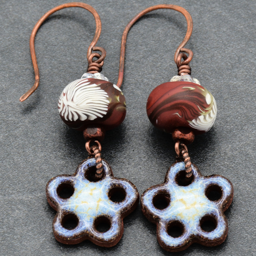 Pair of earrings with floral designs and marbled beads on a gray background