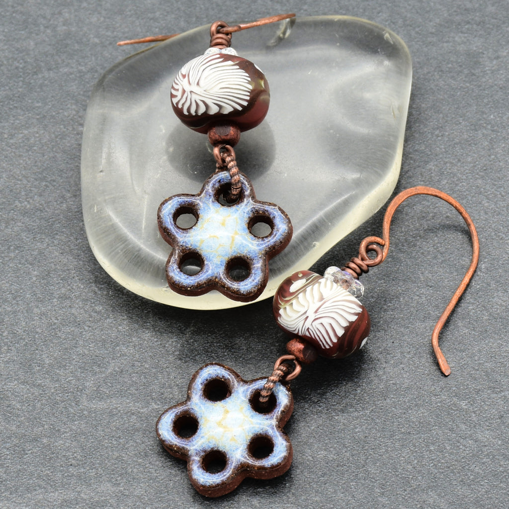 Pair of ceramic flower-shaped earrings with brown and white beads on a gray surface