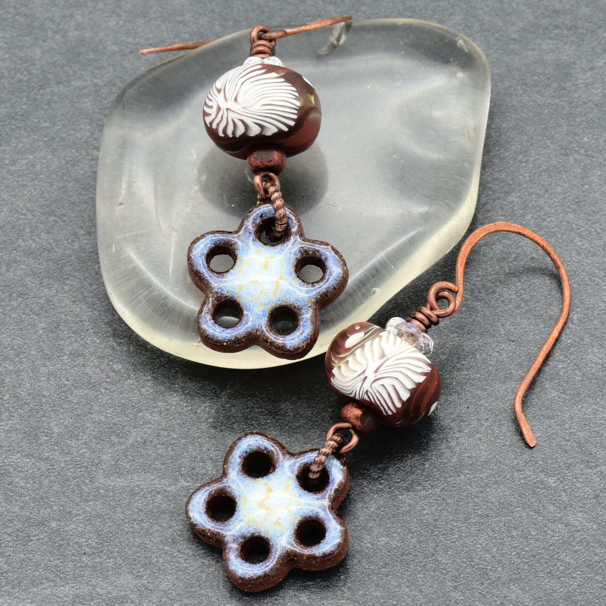 Pair of ceramic flower-shaped earrings with brown and white beads on a gray surface