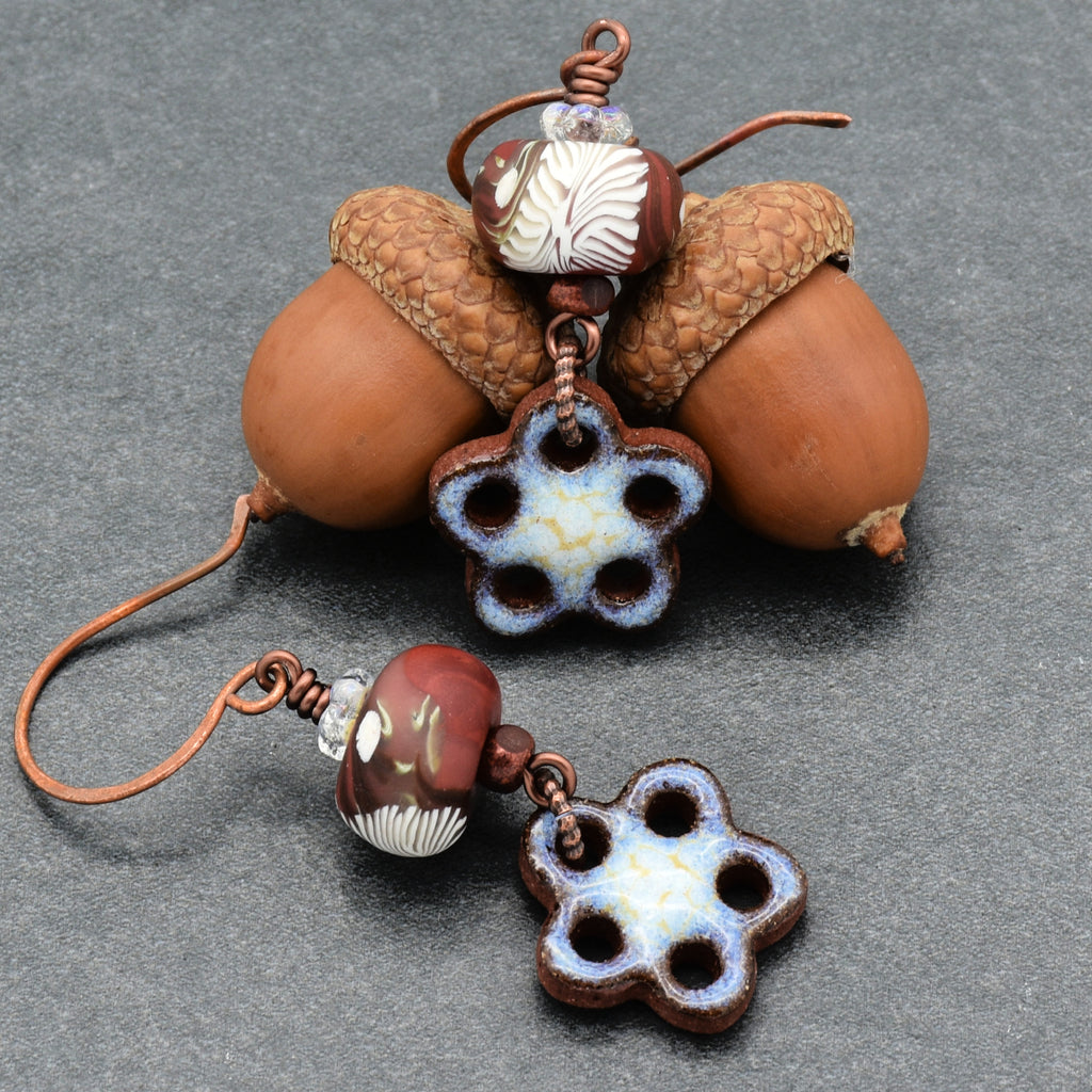 Decorative earrings with brown and white beads and flower-shaped charms on a gray background