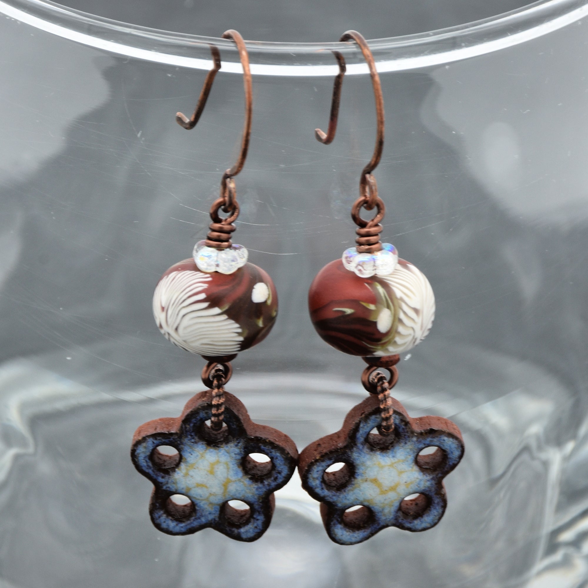 Pair of earrings with marbled beads and flower-shaped pendants on a reflective surface.