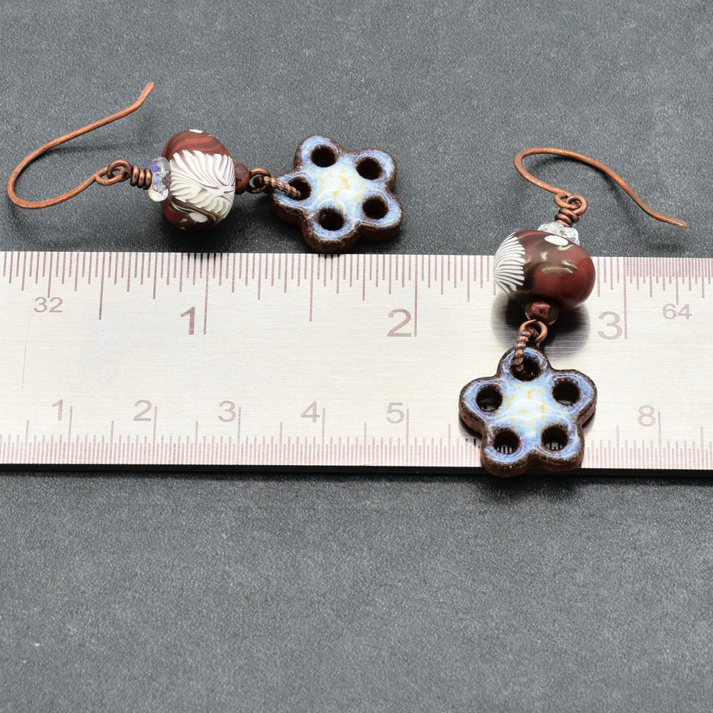Pair of earrings with floral designs and beads on a ruler for scale.