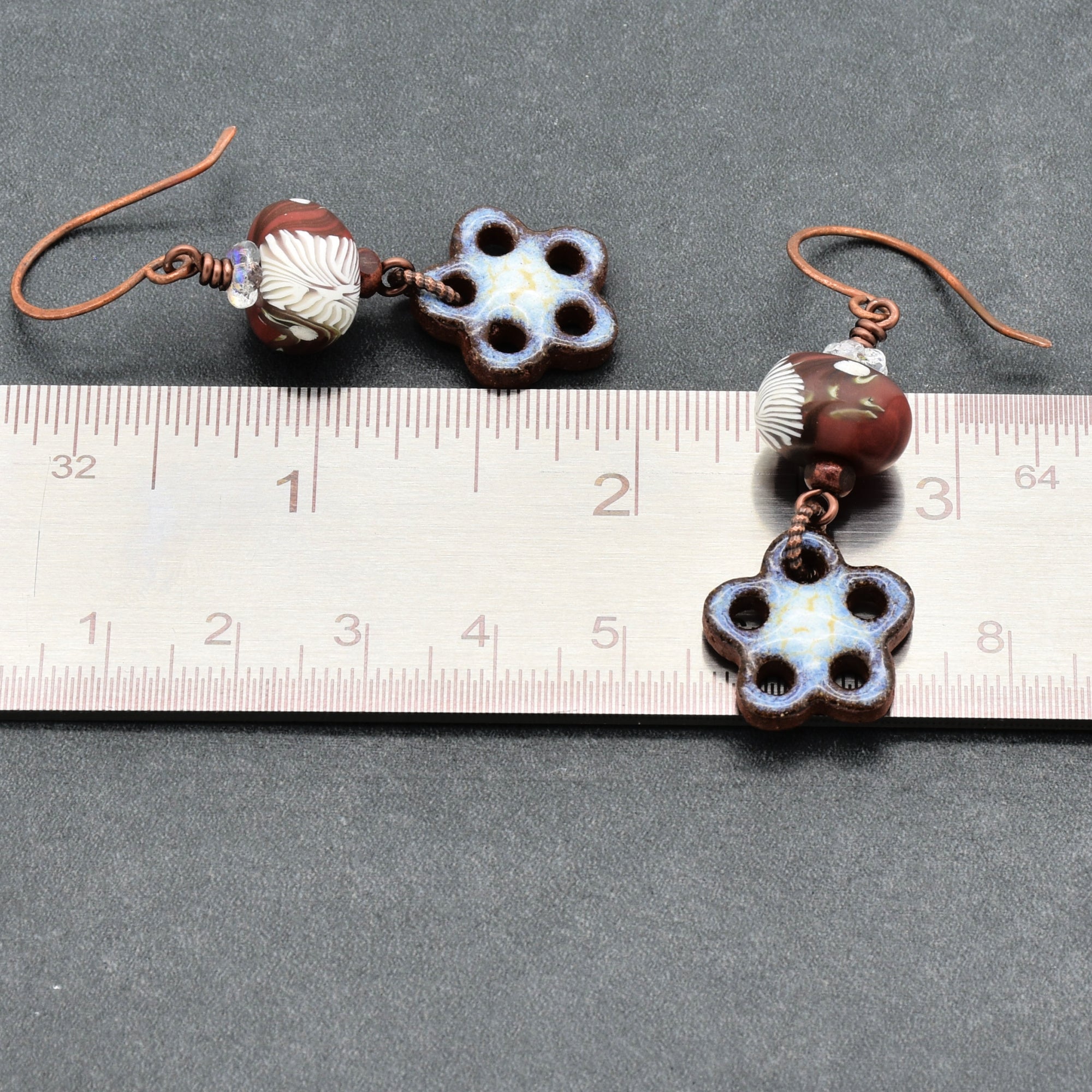 Pair of earrings with floral designs and beads on a ruler for scale.
