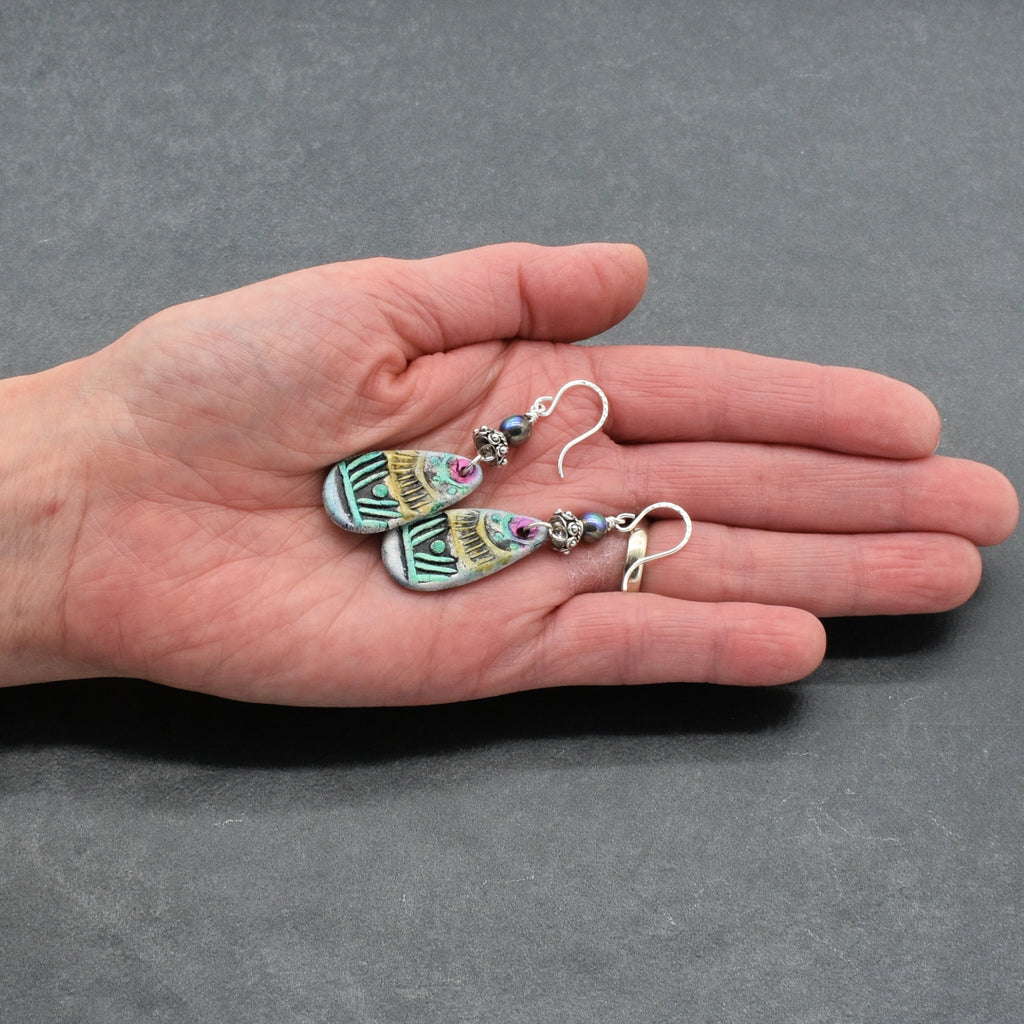 Hand holding colorful earrings against a gray background