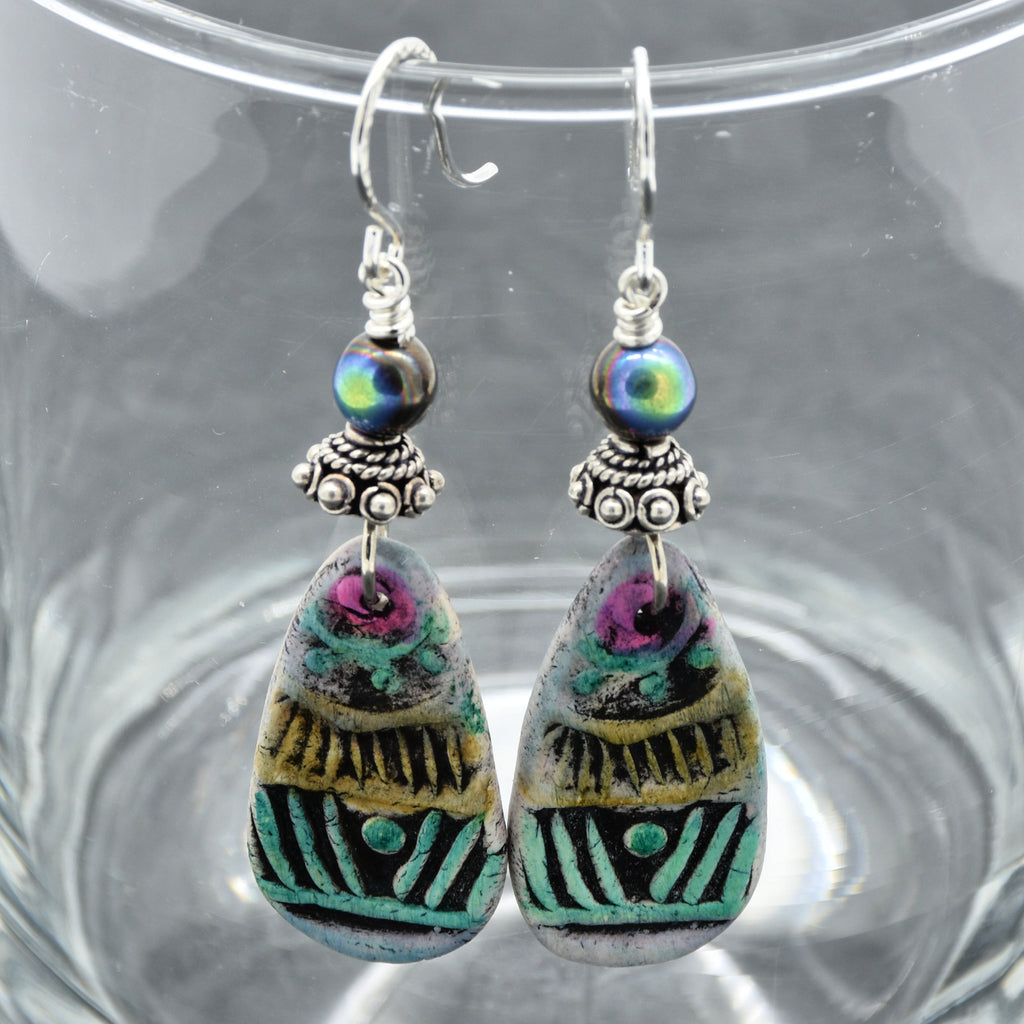 Colorful teardrop-shaped earrings with intricate designs on a glass surface