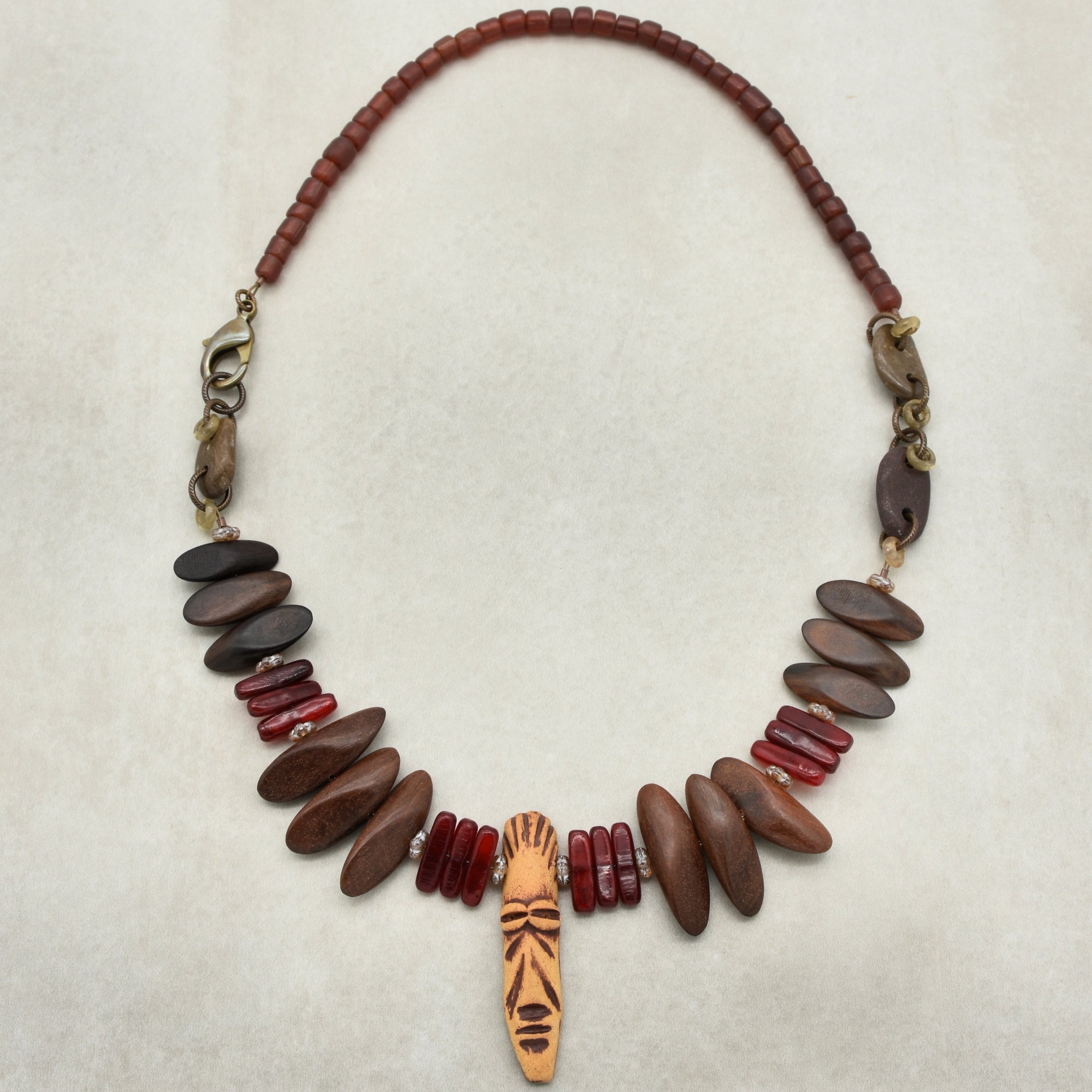 This image shows a necklace. The necklace features a combination of beads, including brown, red, and a central pendant with a carved or painted design.