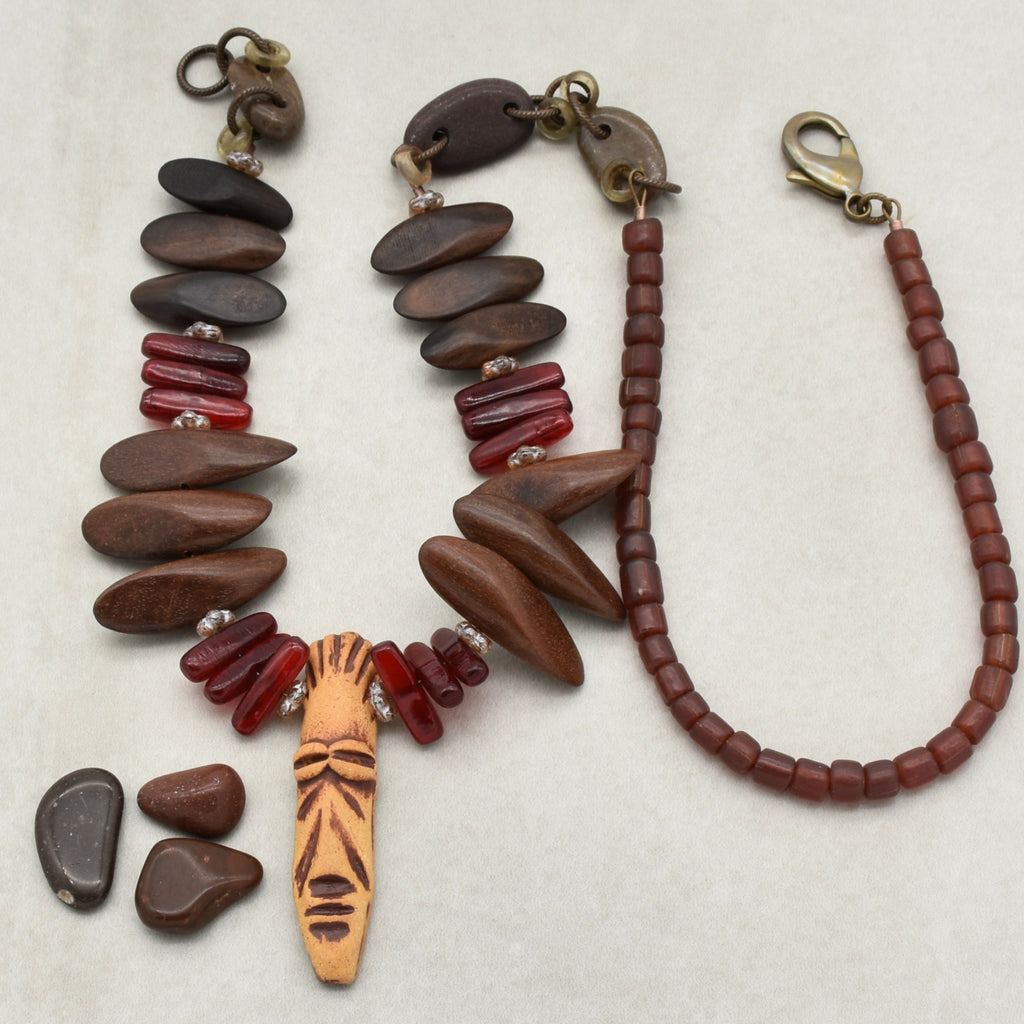 This image shows a necklace. The larger piece on the left with the carved face pendant and a mix of wooden and red beads is characteristic of a necklace. The other item to the right is likely a bracelet given its size and clasp type.