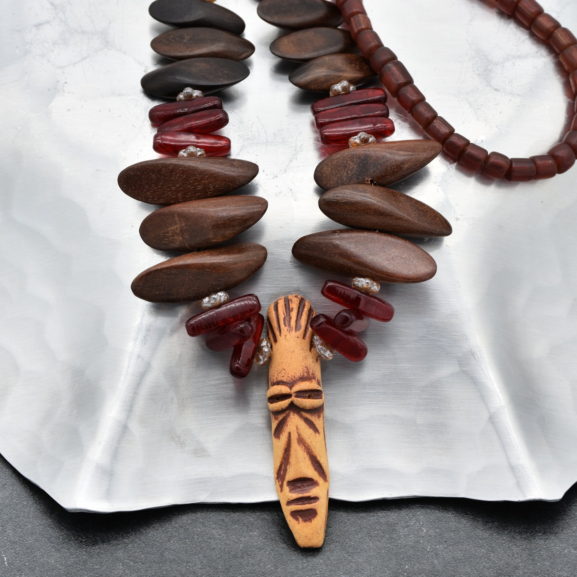 The image shows a necklace. It consists of large brown wooden beads, red beads, and a central pendant that appears to be a carved face. The size and arrangement of the beads, along with the pendant in the center, are characteristic of a necklace.