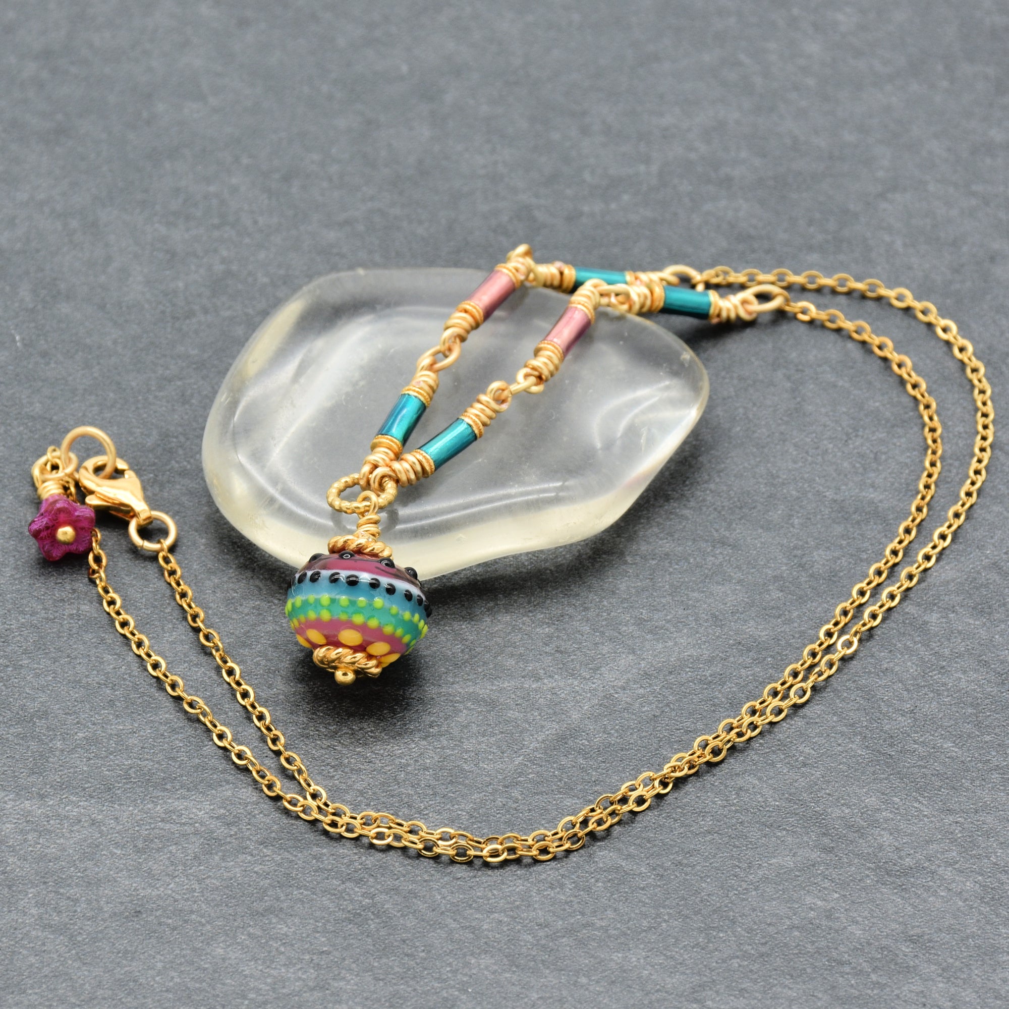 Gold chain necklace with colorful artisan lampwork glass focal and enamel tubes on a gray surface - one of a kind wearable by Ruby Acorn