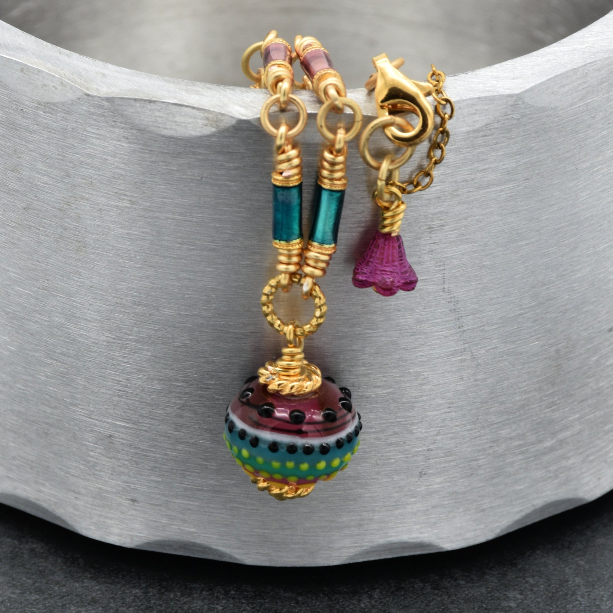 Close up of gold chain necklace with colorful artisan glass focal and enamel tubes on a metallic surface - one of a kind wearable art by Ruby Acorn