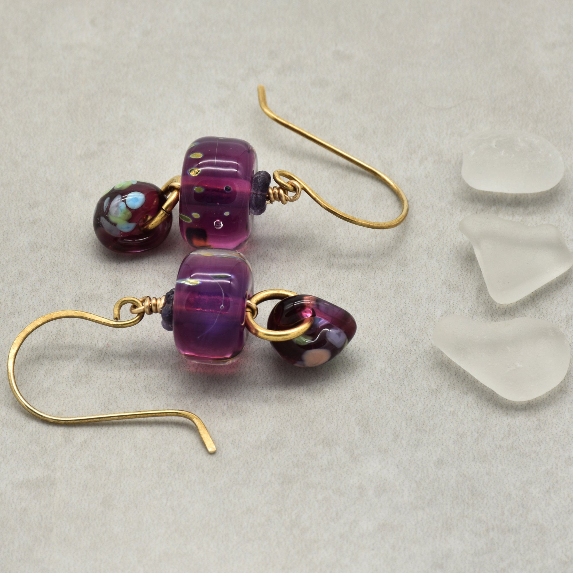 Purple beaded earrings with brass hooks on a light gray background