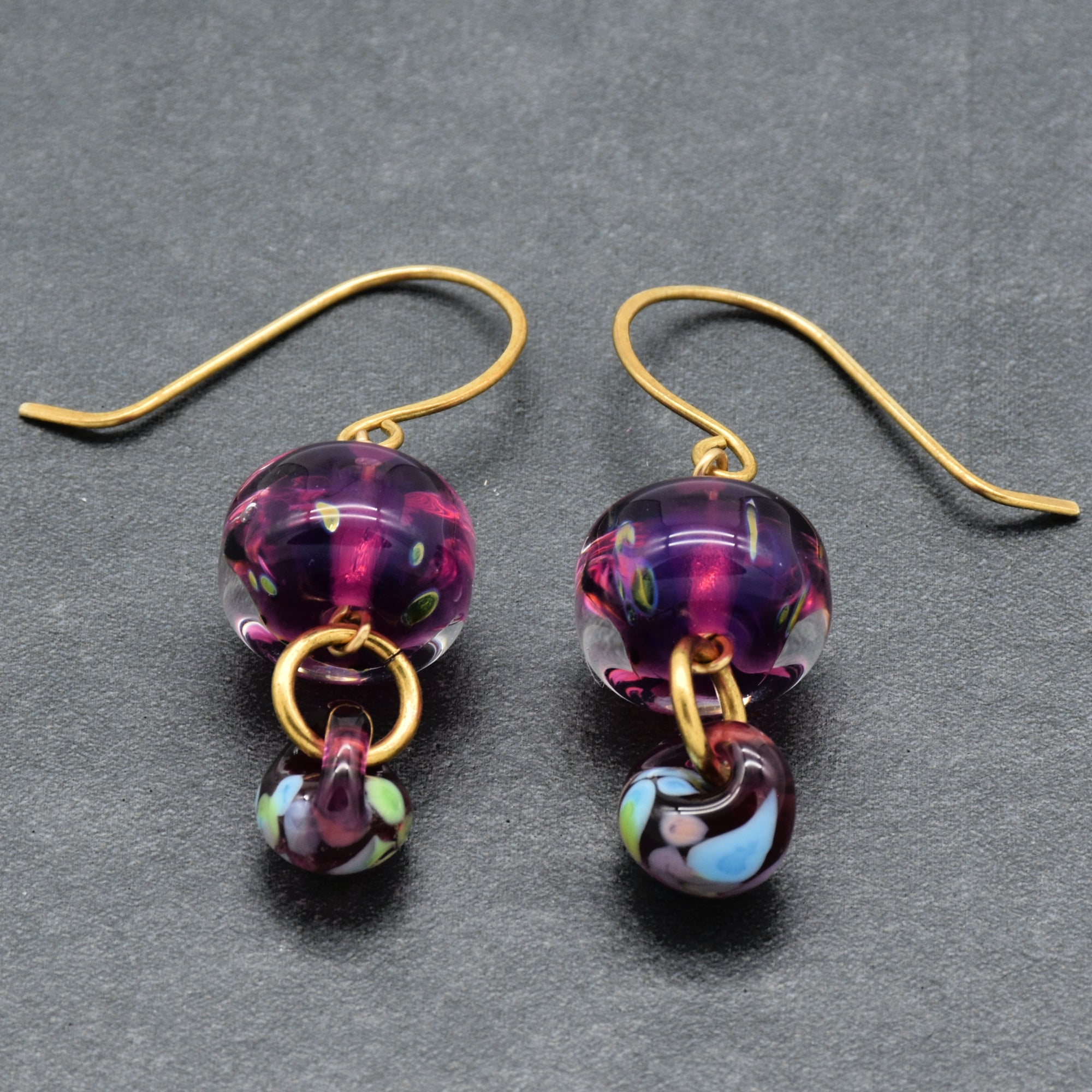 Pair of purple glass bead earrings with brass accents on a gray background