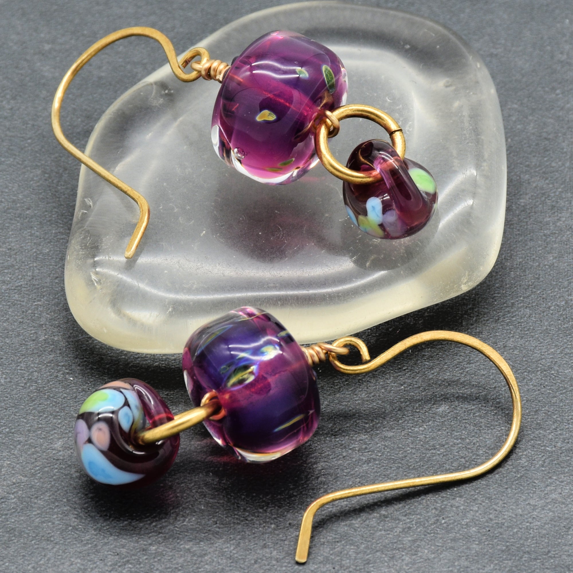 Purple glass bead earrings with brass ear wires on a clear stone background