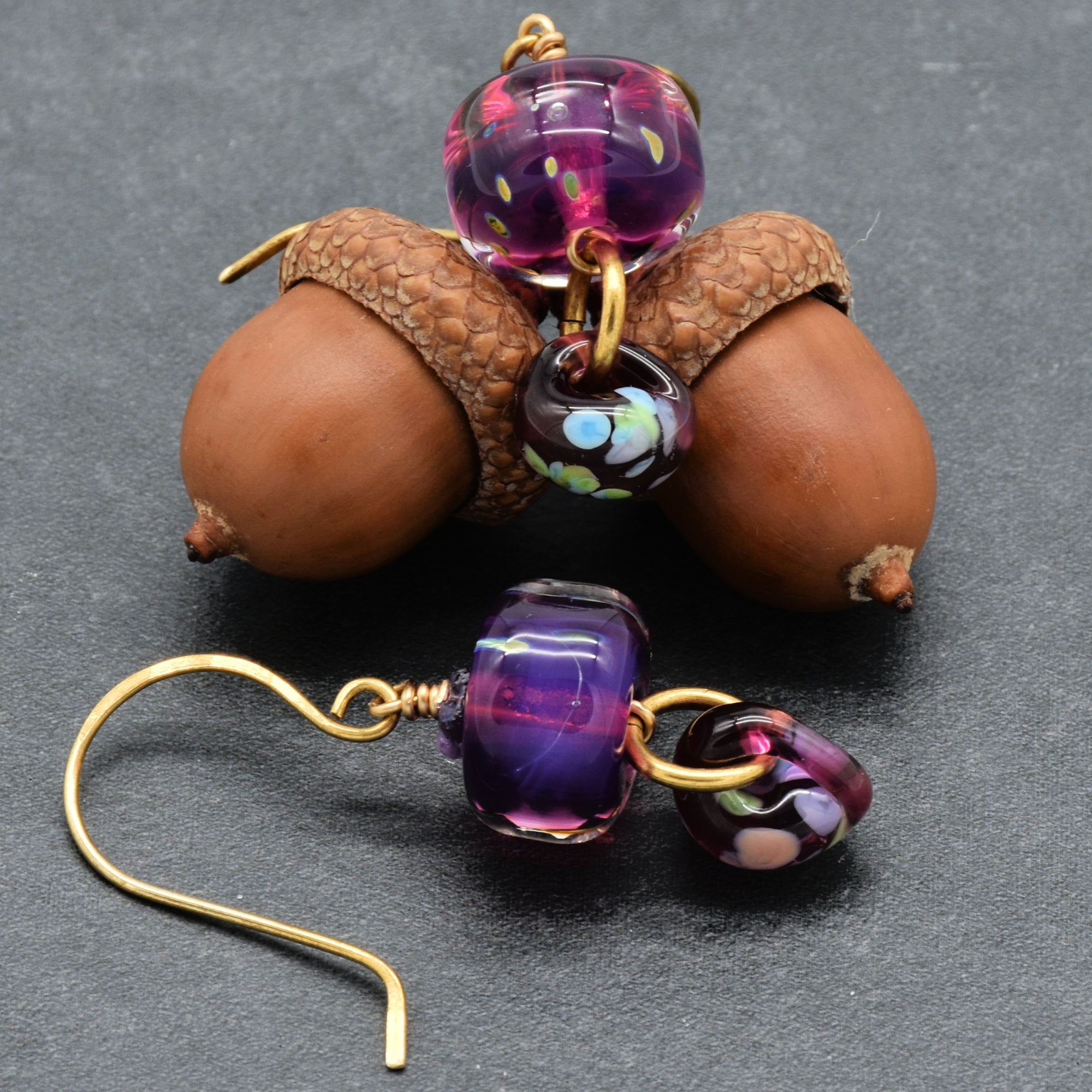Earrings with purple glass beads and brass hooks on a dark background